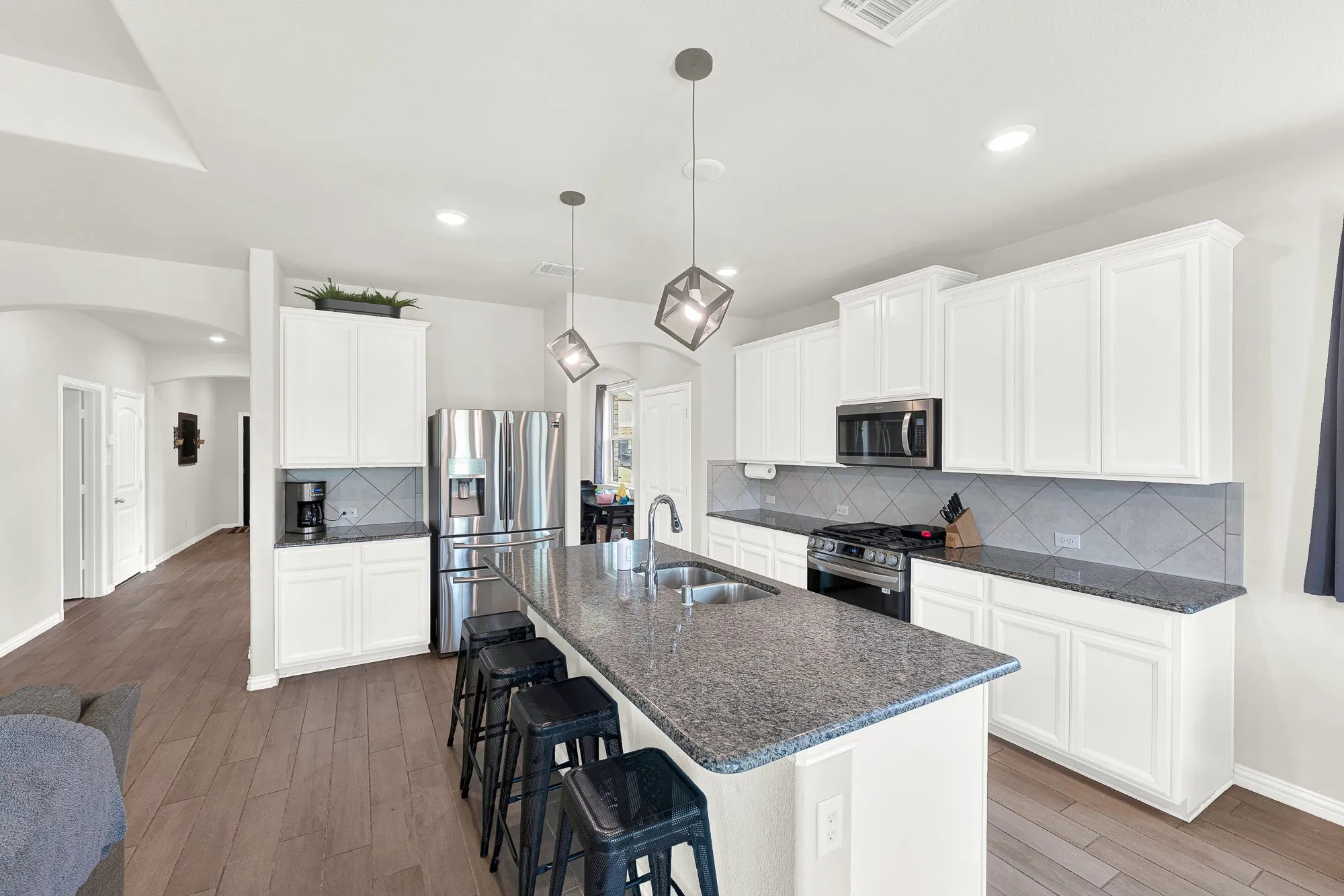 Spacious kitchen featuring an expansive island with a double basin sink, stainless steel appliances, white cabinetry, and granite countertops