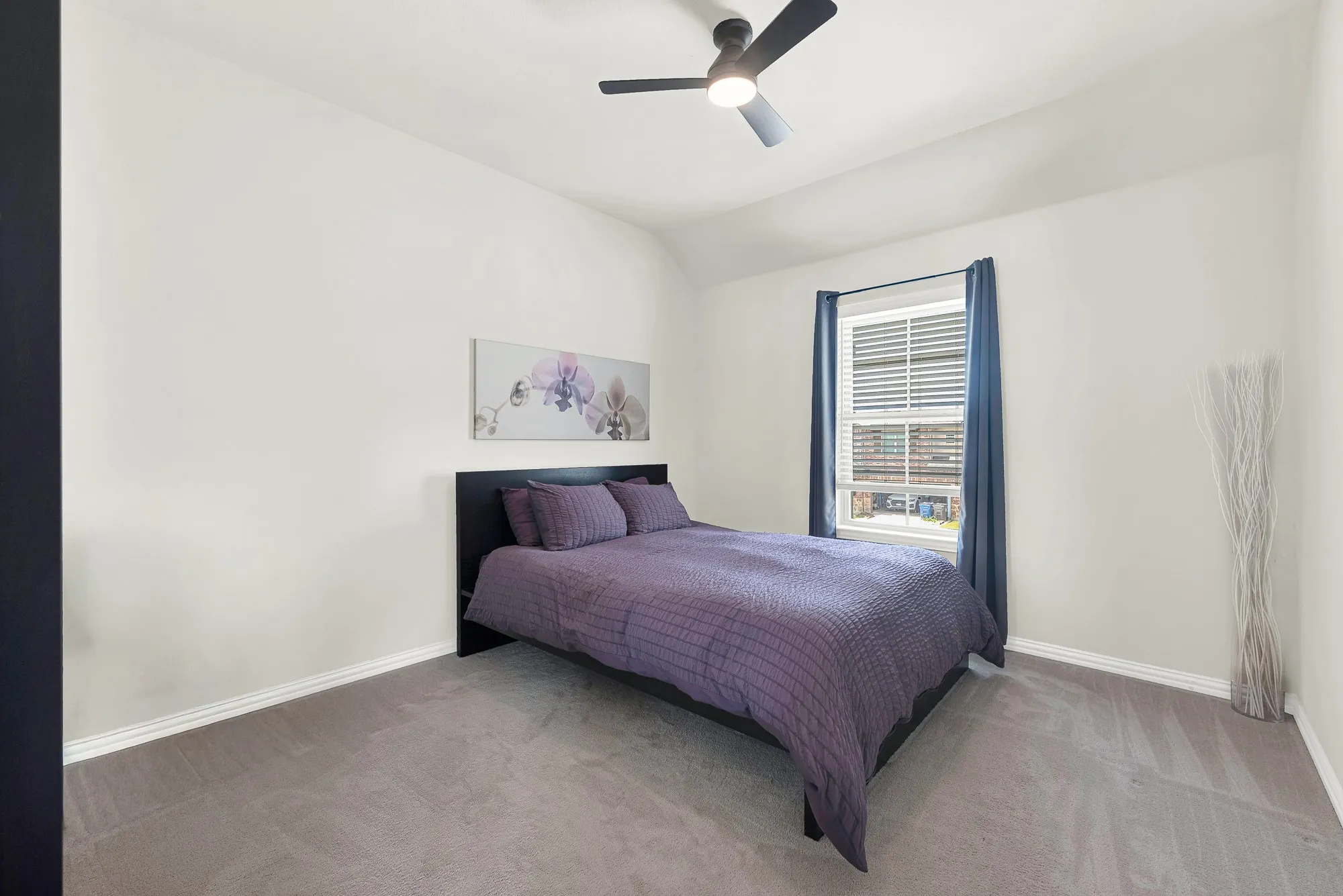 Spacious room featuring vaulted ceilings, a single window with blinds and drapes, a ceiling fan with integrated lighting, white walls, and gray carpet flooring