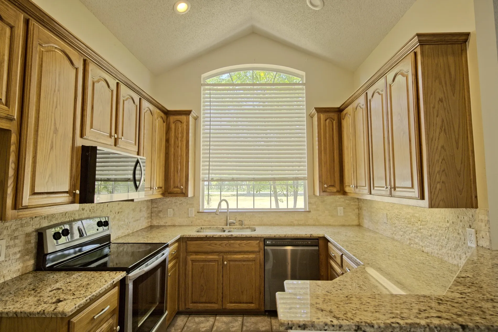 U-shaped kitchen featuring wood cabinetry with crown molding, light-toned countertops, tile backsplash, and a stainless steel dishwasher