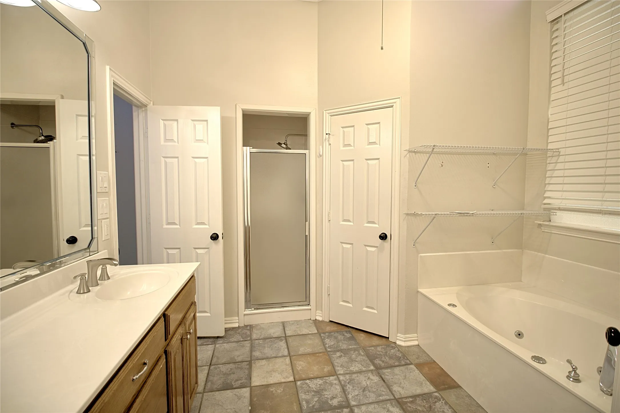 Bathroom featuring a built-in jetted tub, a separate shower with a frosted glass door, and a single vanity with wood cabinetry