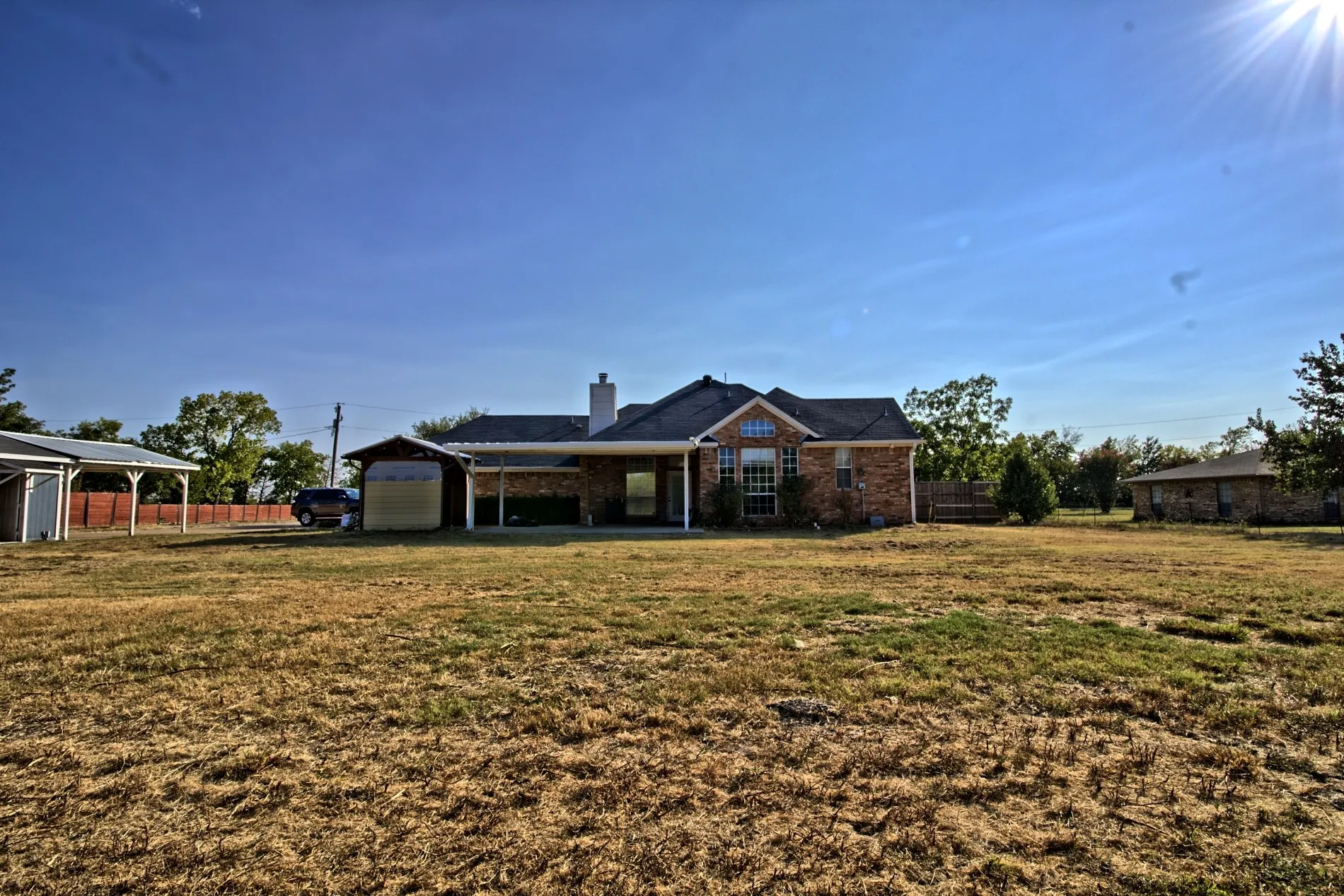 Expansive property featuring a brick exterior residence with a covered patio, an attached carport, and a detached outbuilding