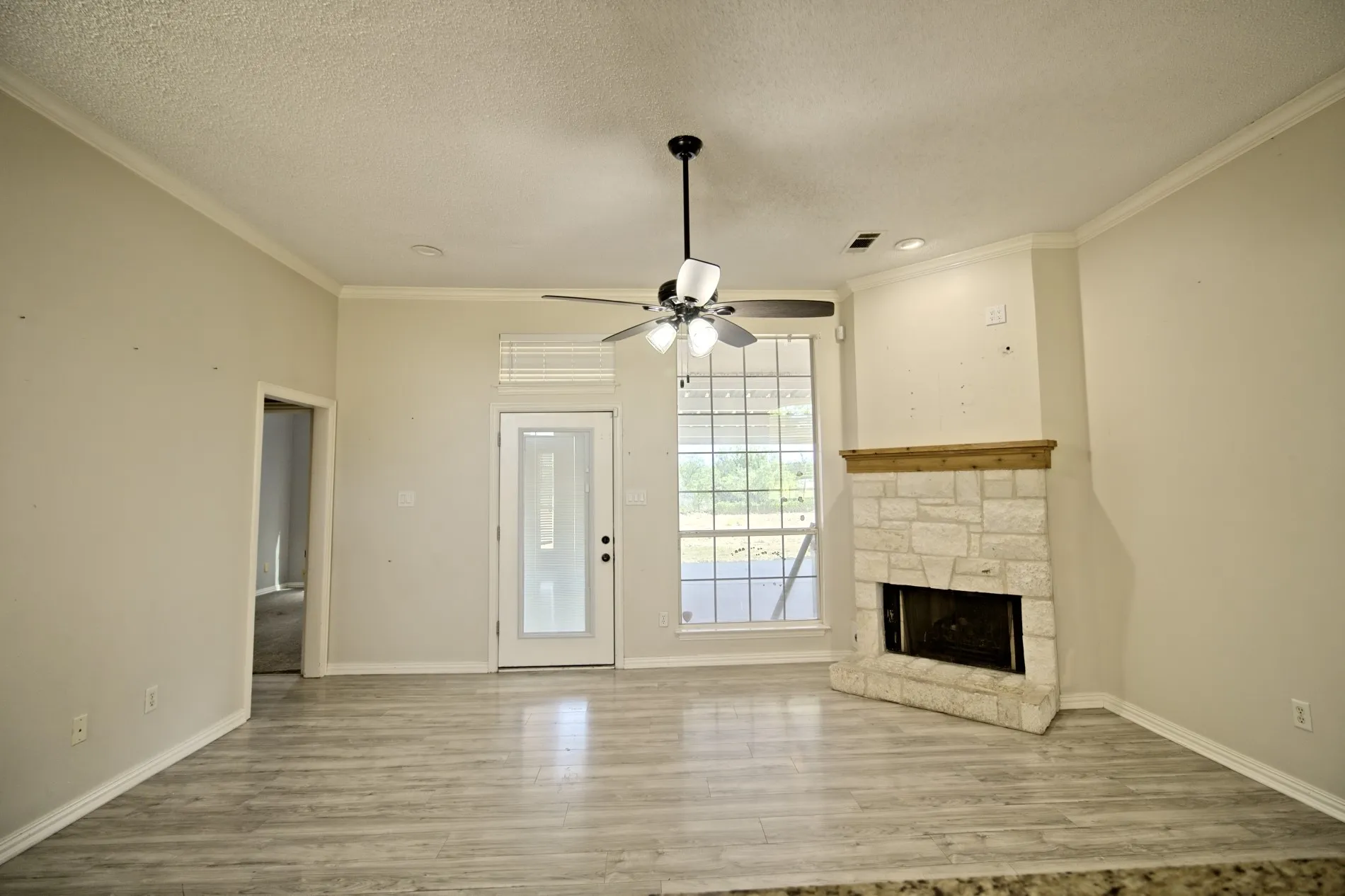 Living area featuring wood-finish flooring, a stone-clad fireplace with a wood mantle, and a ceiling fan with integrated lighting