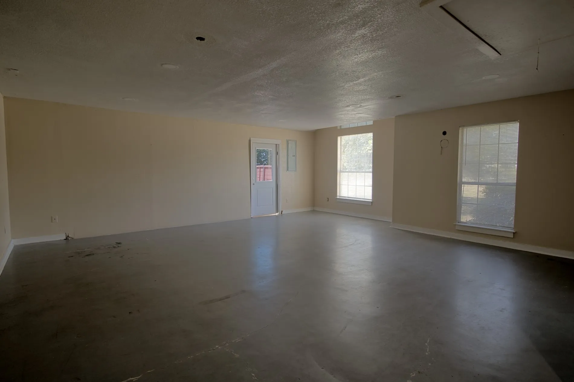 Spacious room featuring neutral paint, multiple windows, a white door, and textured ceilings