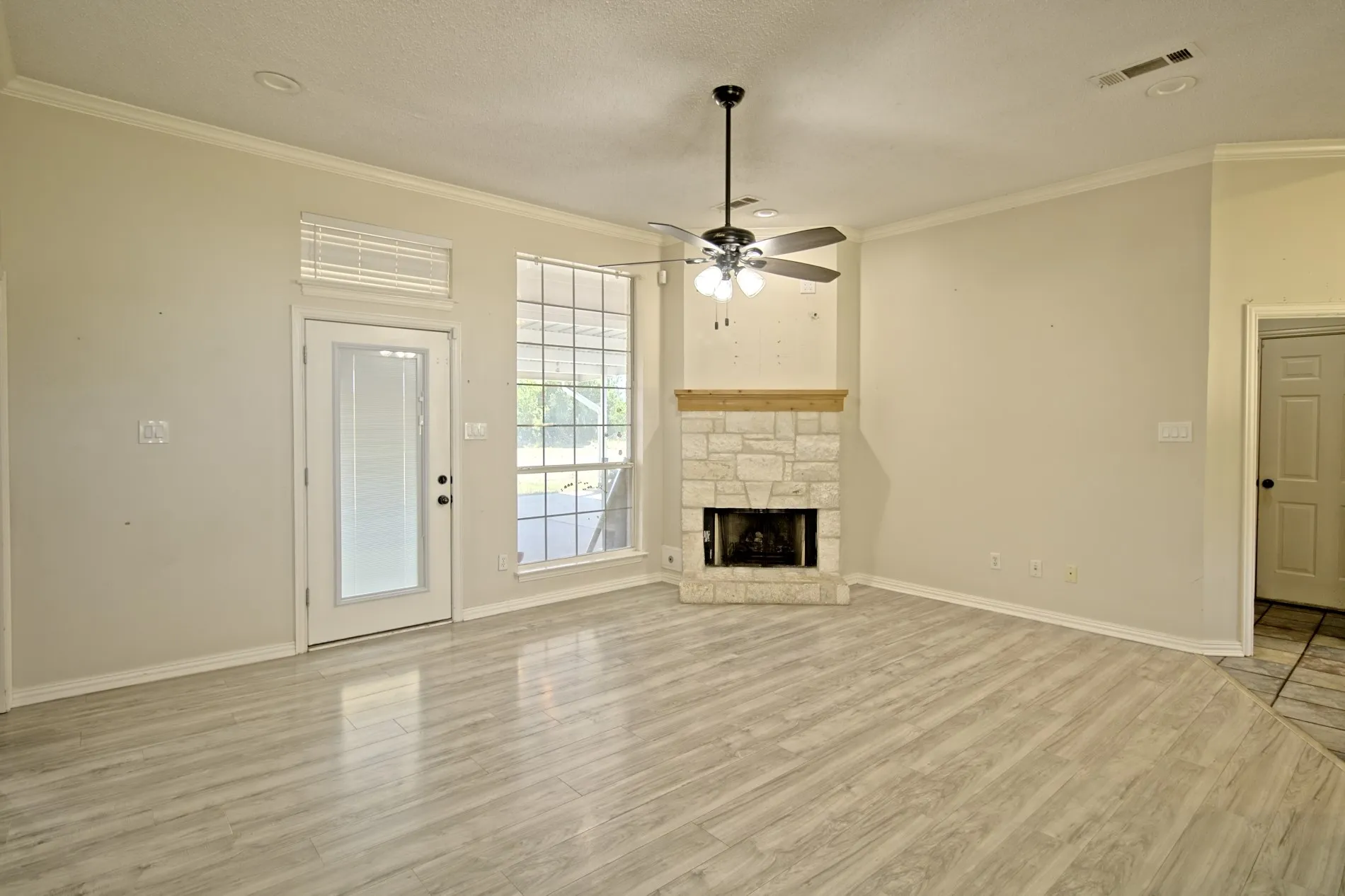 Spacious room featuring wood-finish flooring, a stone fireplace with a wood mantle, and a ceiling fan