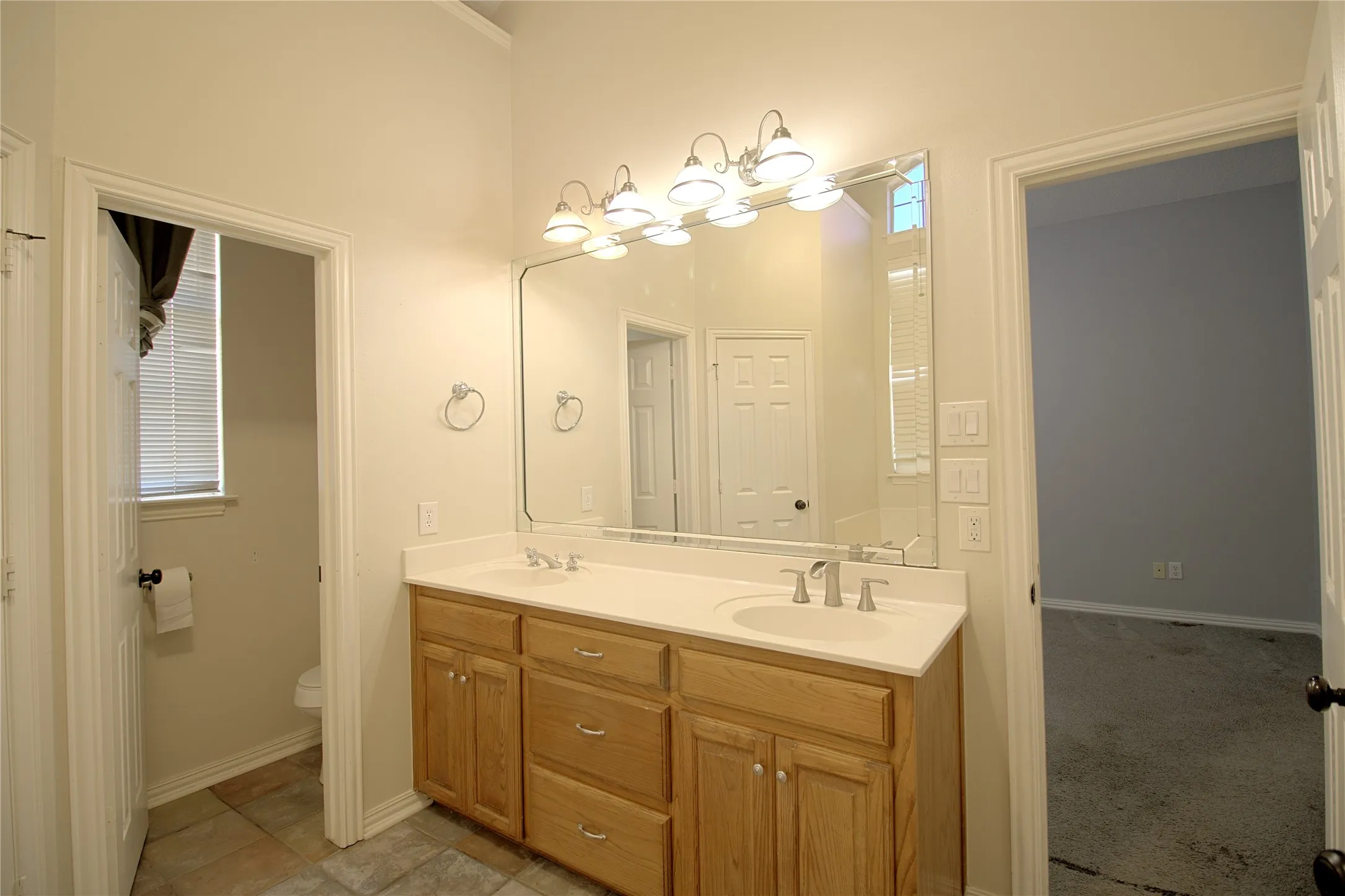 Bathroom vanity featuring a light wood cabinet with ample storage, dual sinks, a large mirror, and a multi-bulb light fixture