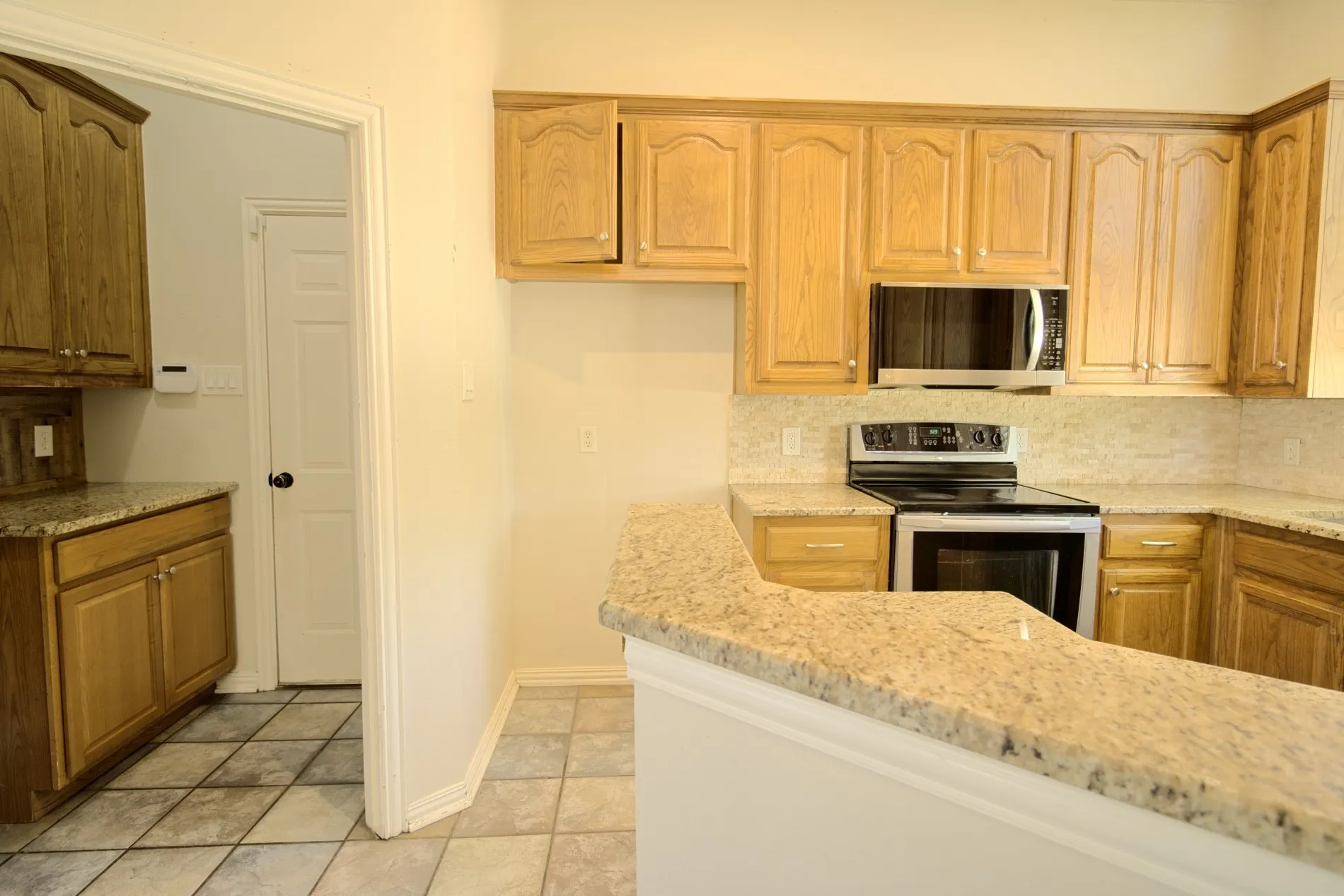 Kitchen featuring light wood cabinetry, stone countertops, stainless steel appliances, and a tiled backsplash