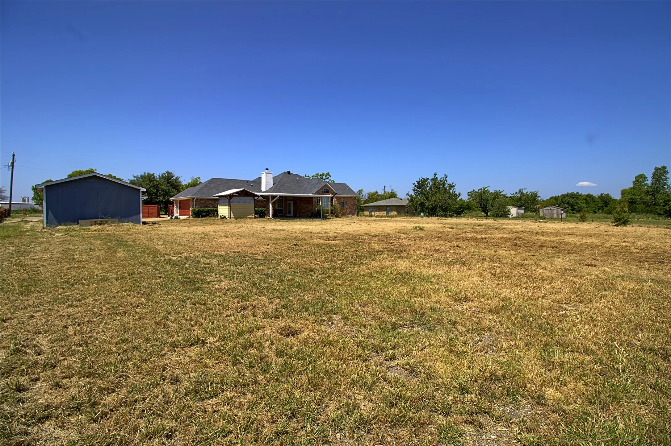 Expansive open field with scattered dry grass and distant residential structures