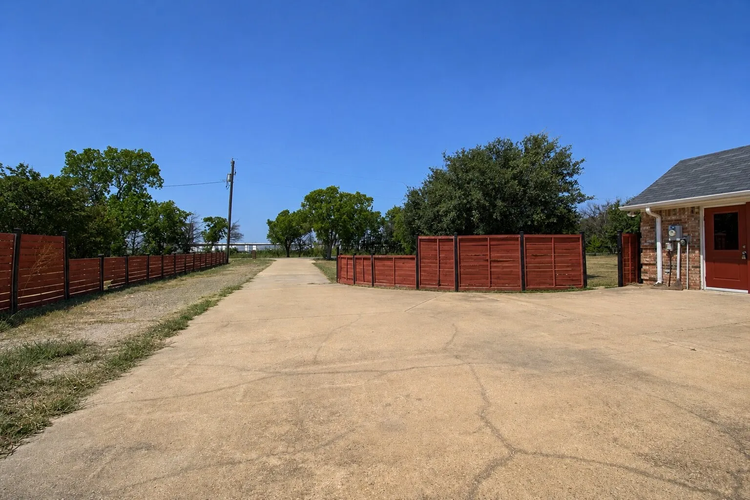 Concrete driveway with a wood-stained fence and mature trees