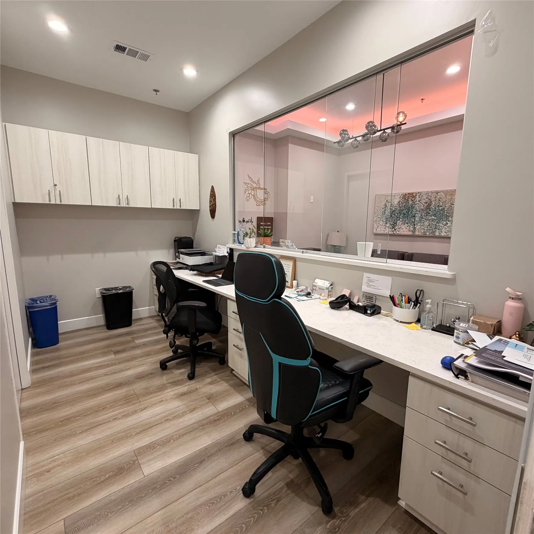 Spacious office area featuring wood-finish flooring, recessed lighting, and a full wall of light-toned cabinetry with silver hardware