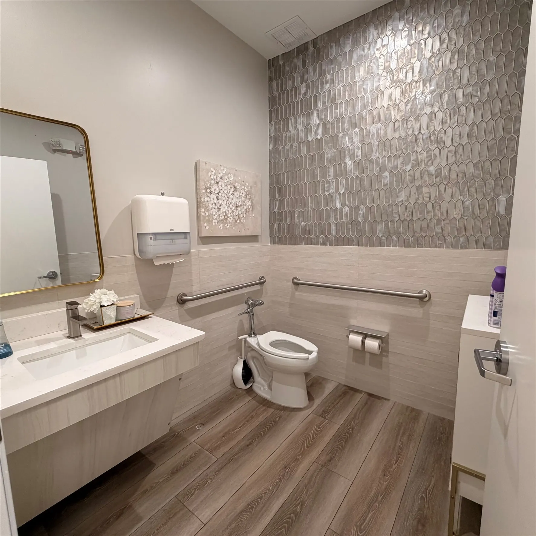 Bathroom featuring a modern vanity with integrated sink, gold-framed mirror, wood-finish flooring, and decorative accent wall tile