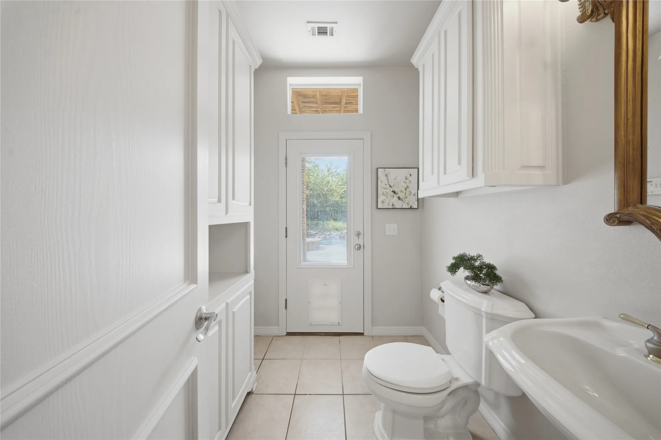 Integrated storage cabinetry featuring open shelving and paneled doors, ceramic tile flooring, and a rear exterior door with an upper transom window