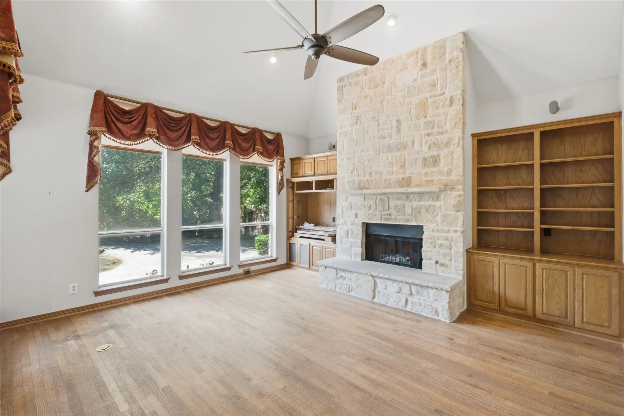 Living area featuring a stone fireplace with hearth, wood-finish flooring, vaulted ceiling, and a ceiling fan
