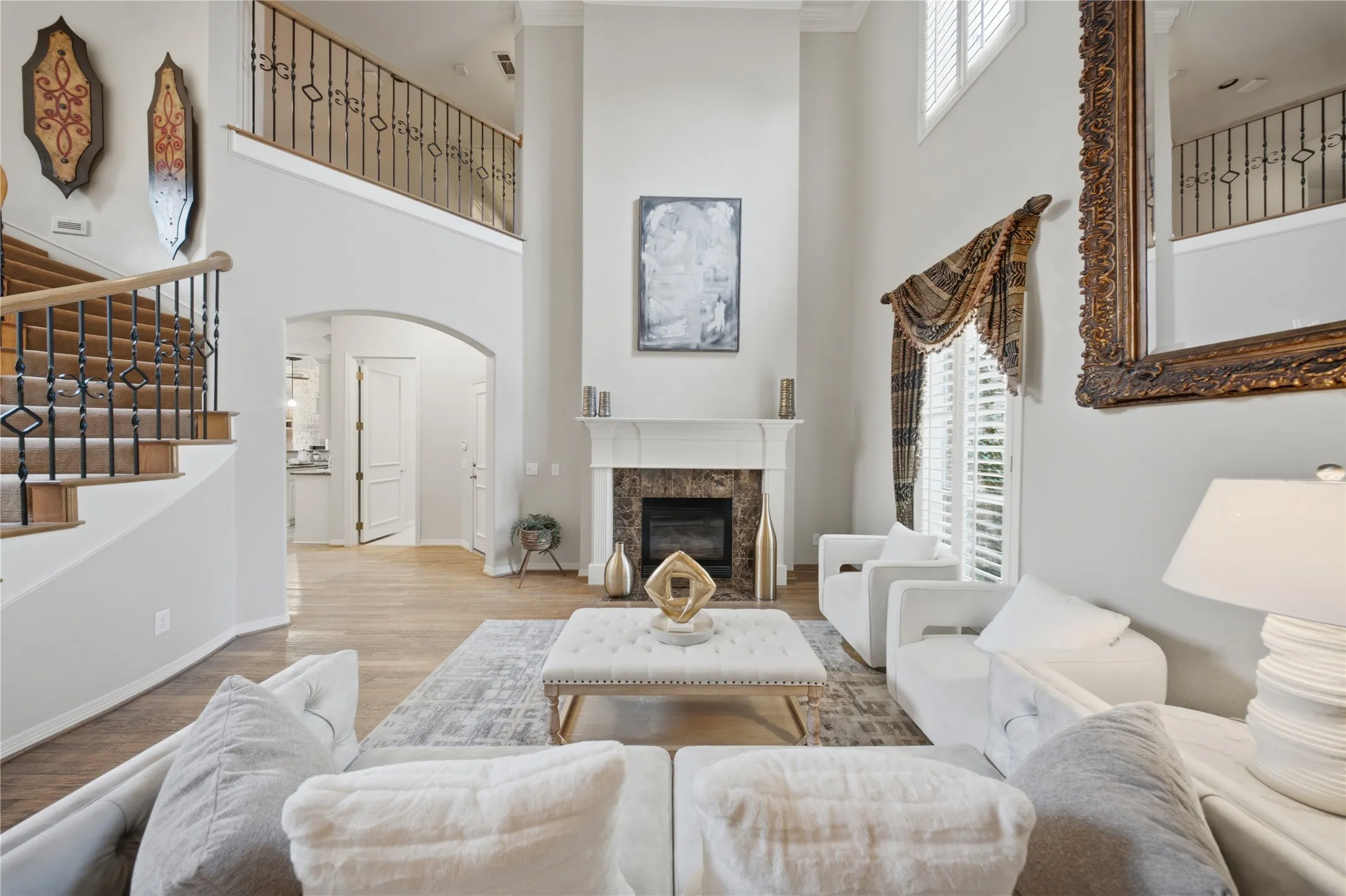 Two-story living area featuring a fireplace with a stone surround and white mantel, wood-finish flooring, plantation shutters, and a staircase with wrought iron balusters