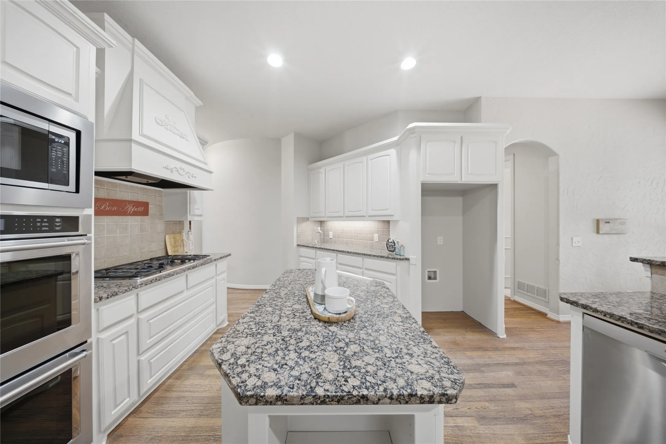Kitchen featuring a granite-topped island, white cabinetry, stainless steel appliances, and wood-finish flooring