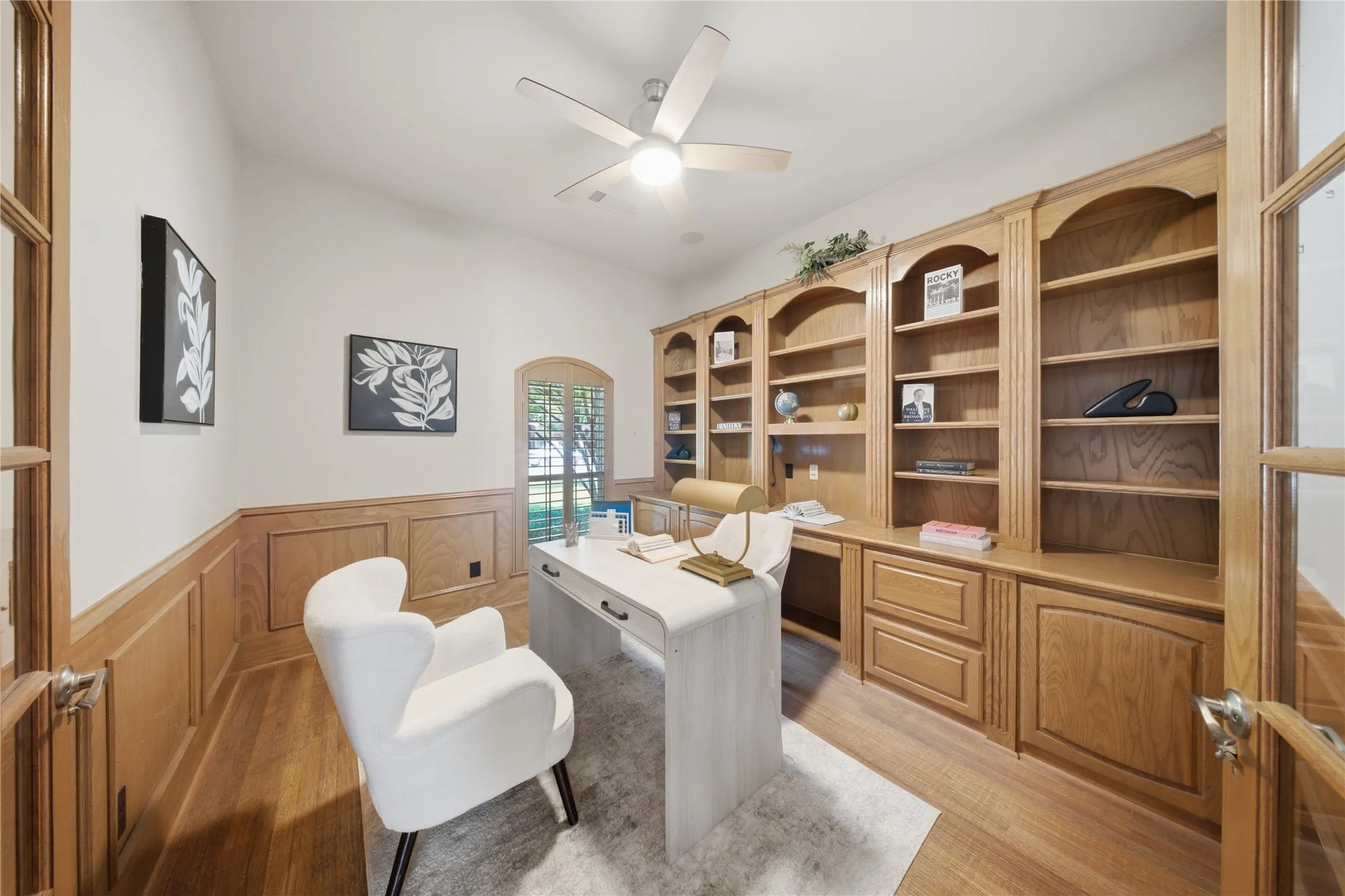 Room featuring extensive built-in wooden shelving and cabinetry, wood-finish flooring, and wainscoting