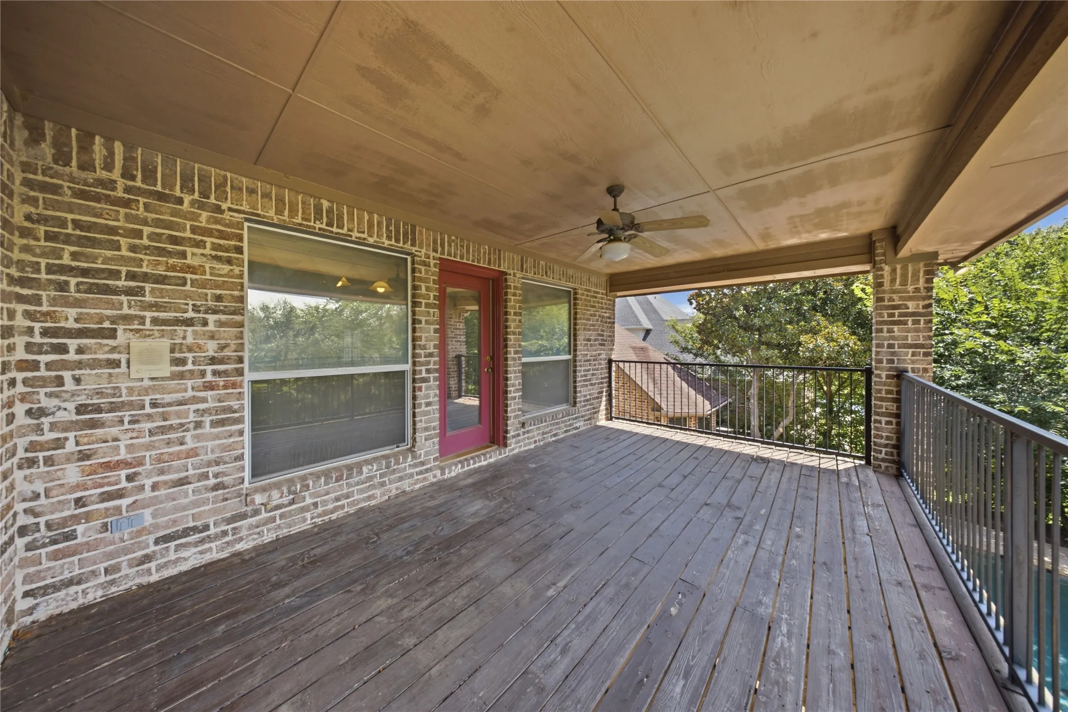 Covered outdoor deck with wood-finish flooring, brick exterior wall, and iron railings
