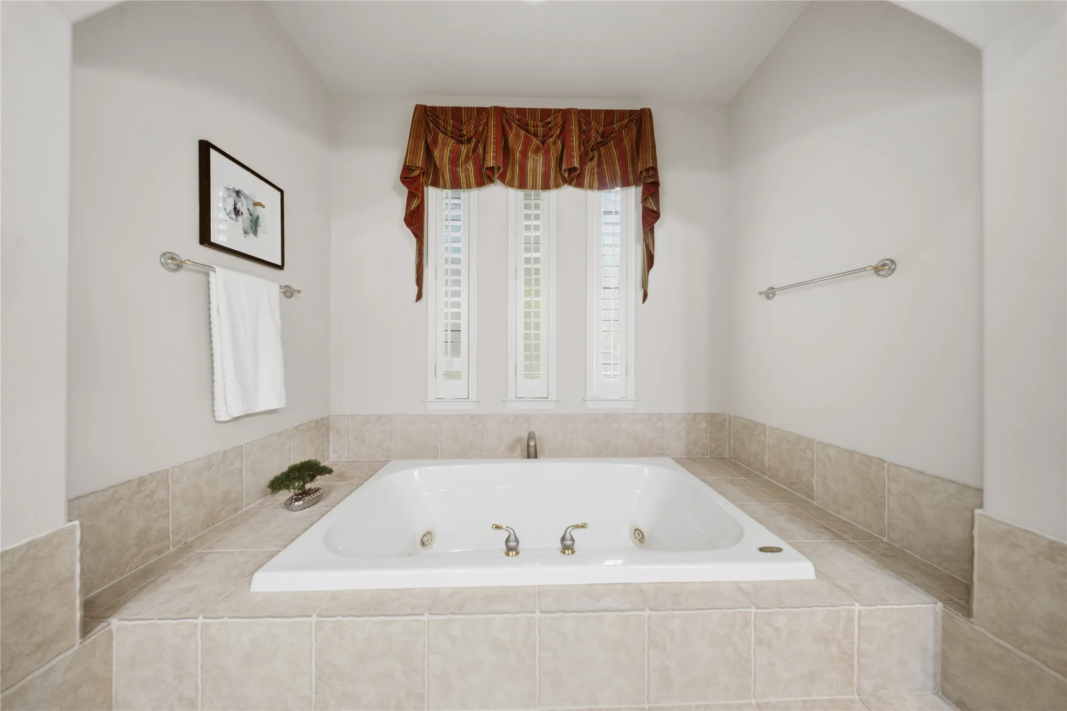 Soaking tub with a tiled surround, integrated brass fixtures, and shuttered windows