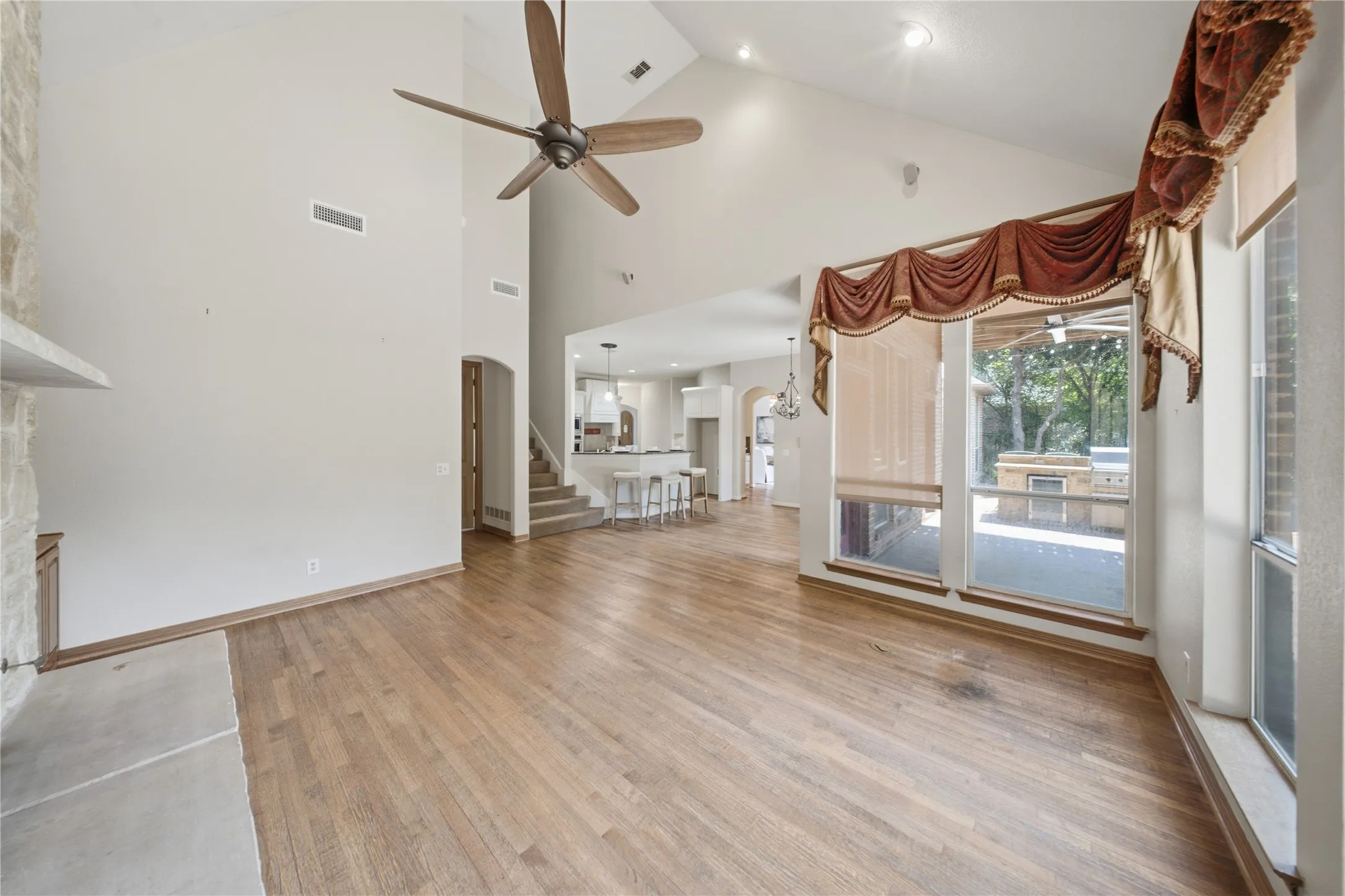 Spacious living area featuring high vaulted ceilings, light wood-finish flooring, a stone fireplace surround with a hearth, and large windows with transom details