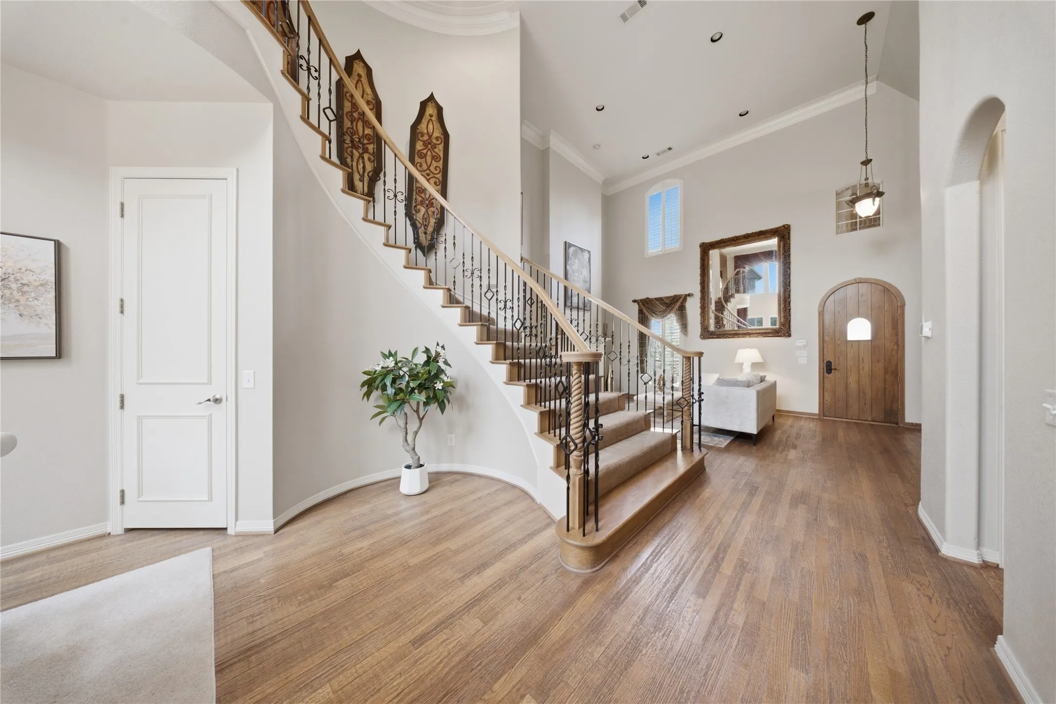 Grand foyer featuring a curved staircase with wrought iron balusters and wood-finish handrails, high ceilings, wood-finish flooring, and an arched wood door