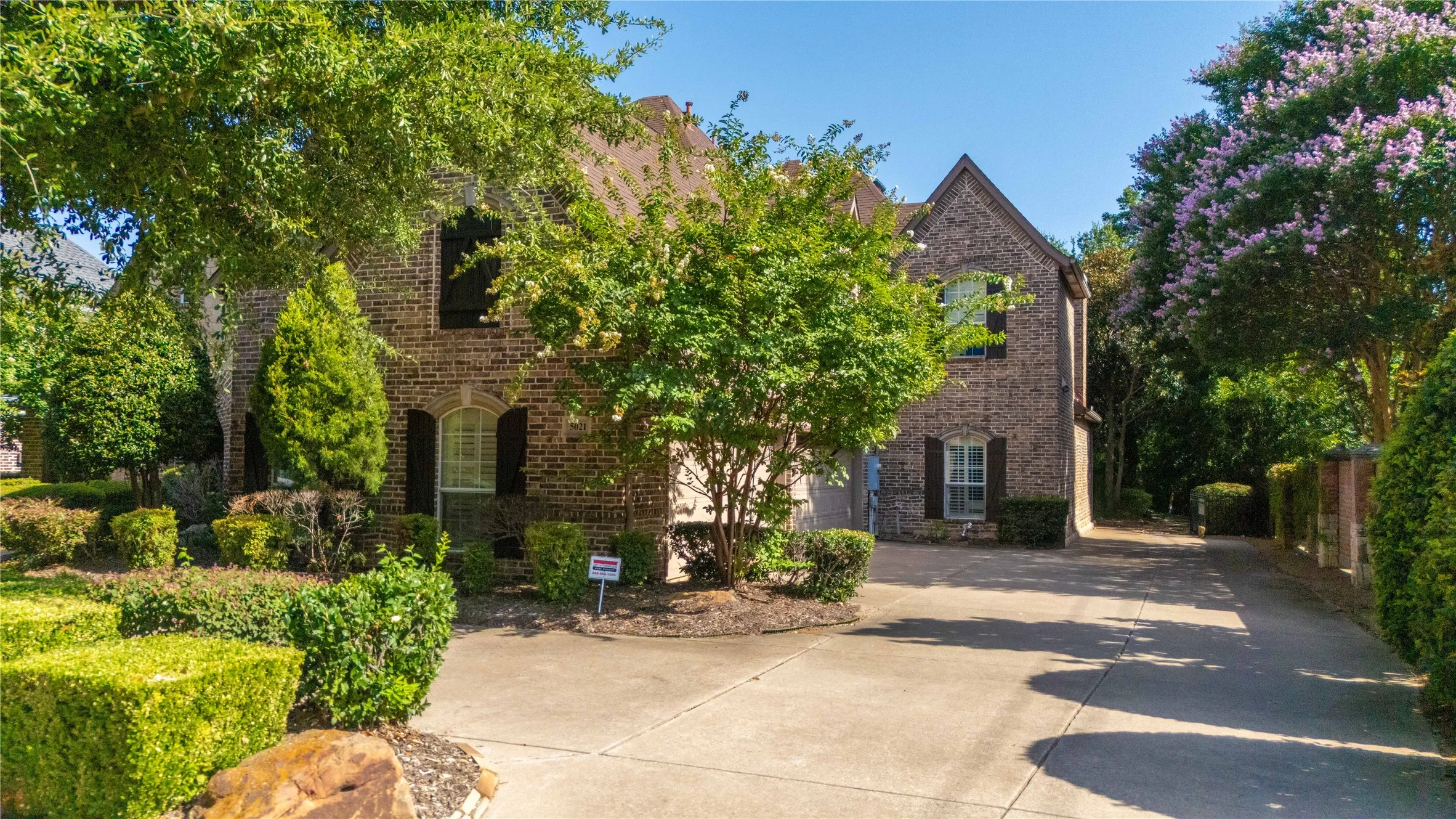 Traditional brick exterior featuring arched windows, dark shutters, and a concrete driveway