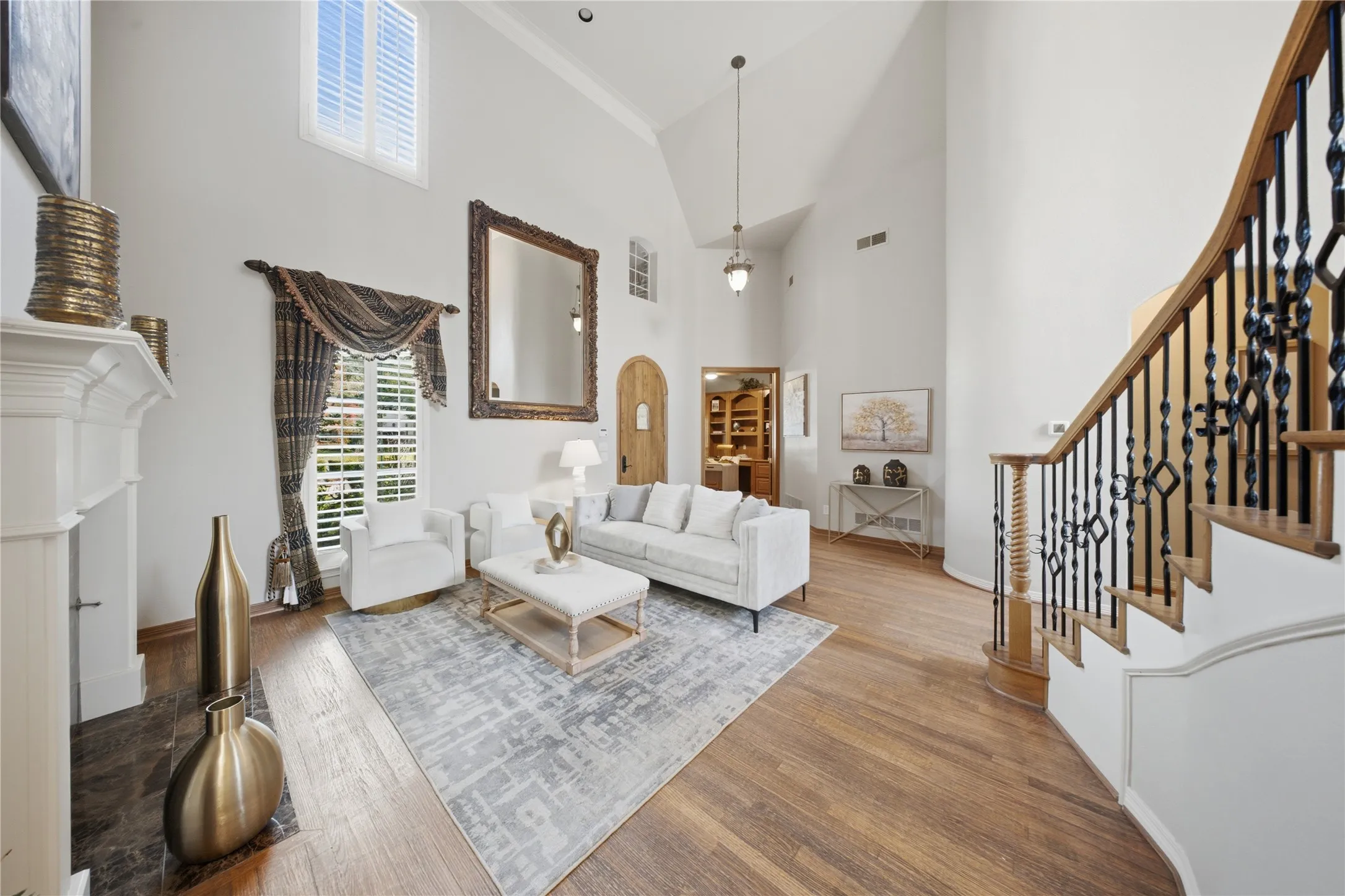 Two-story living area featuring wood-finish flooring, a white mantel, and a staircase with an ornamental iron railing