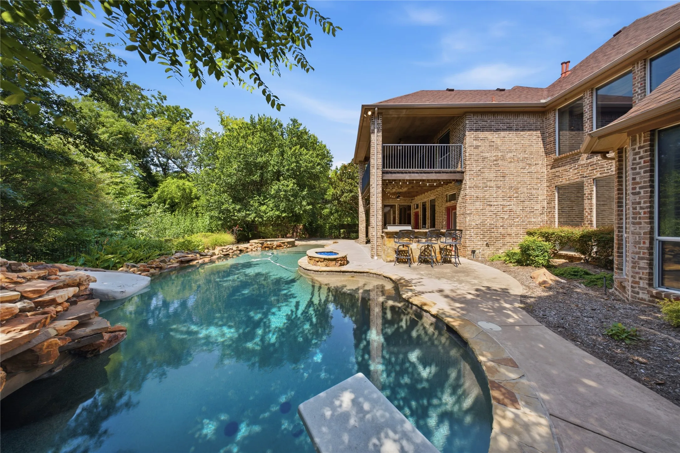 Brick exterior with multiple windows, concrete patio, and a multi-level pool featuring stone accents and a spa