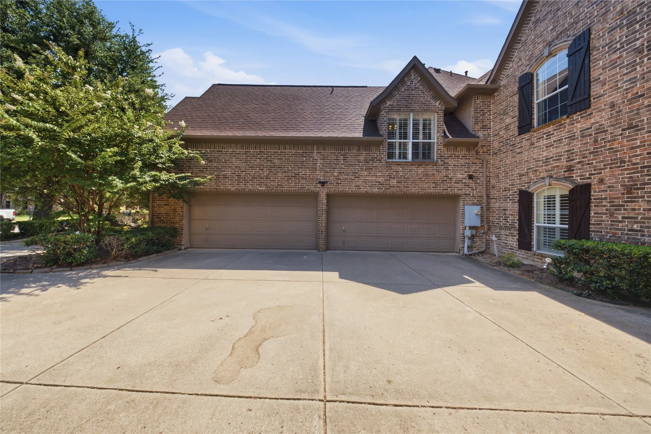 Brick exterior featuring a two-car garage with individual doors, a concrete driveway, and mature landscaping
