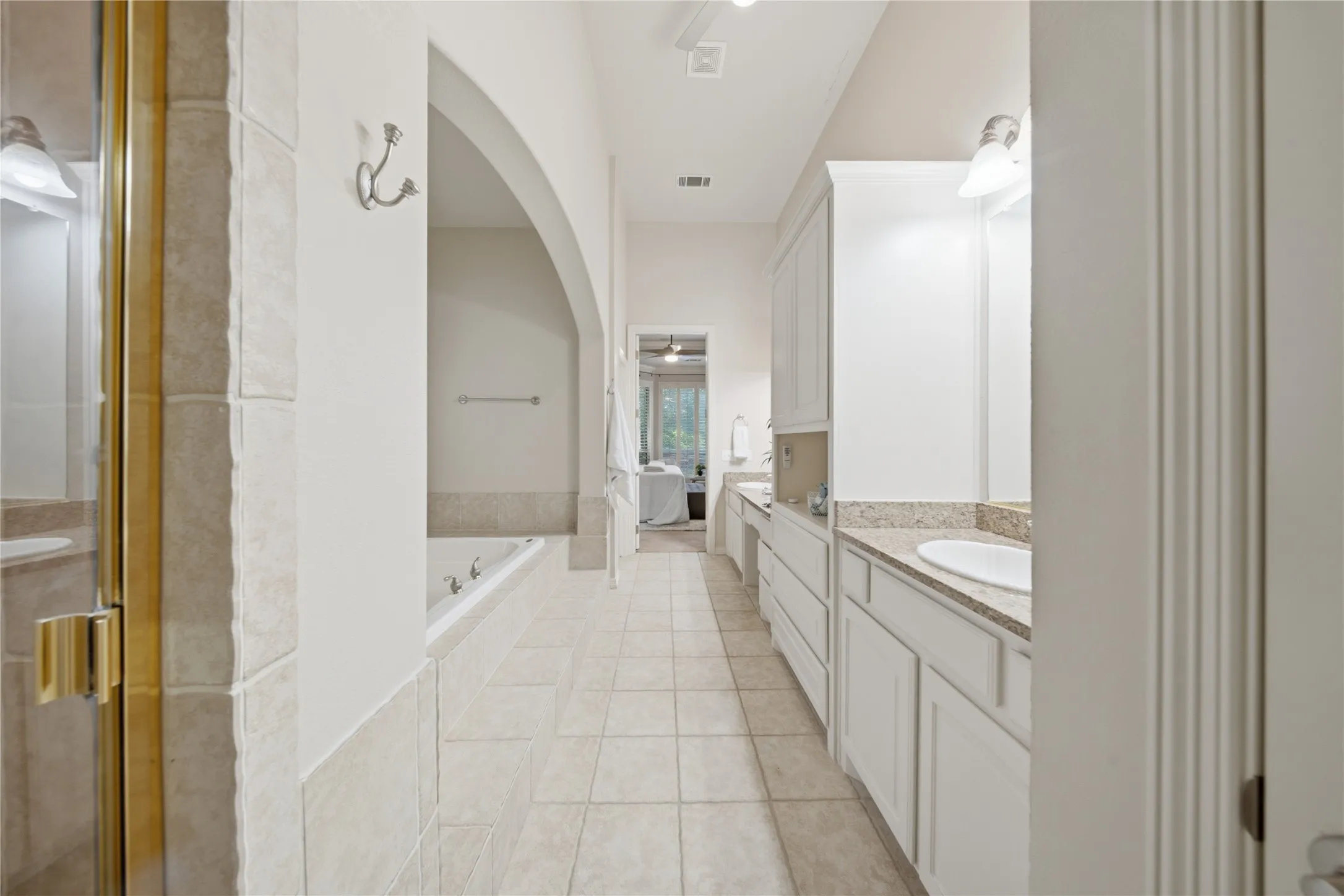 Bathroom featuring a built-in tub, separate shower with brass-finish framing, dual vanity with undermount sinks, and a built-in makeup vanity
