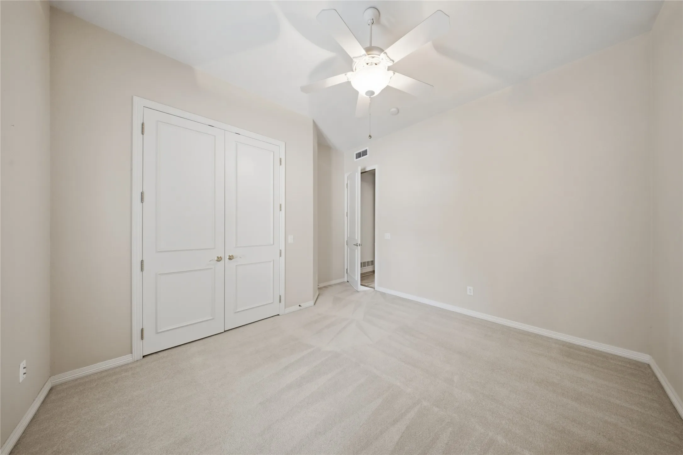 Neutral-toned wall finish, plush carpet flooring, ceiling fan with integrated lighting, and white paneled doors