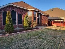 Brick exterior with arched window, manicured shrubbery, and a paved patio featuring a gazebo