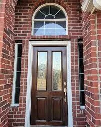 Brick facade entry featuring a dark wood-finish door with glass panels, flanked by sidelight windows and topped with an arched transom window
