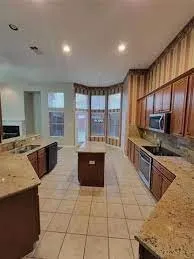 Kitchen featuring a central island, recessed lighting, tile flooring, wood cabinetry, and extensive light-toned countertops