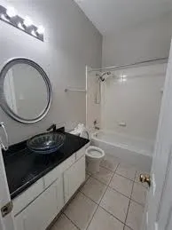Bathroom featuring a single vanity with a dark countertop and vessel sink, a round mirror, and a built-in shower-over-tub