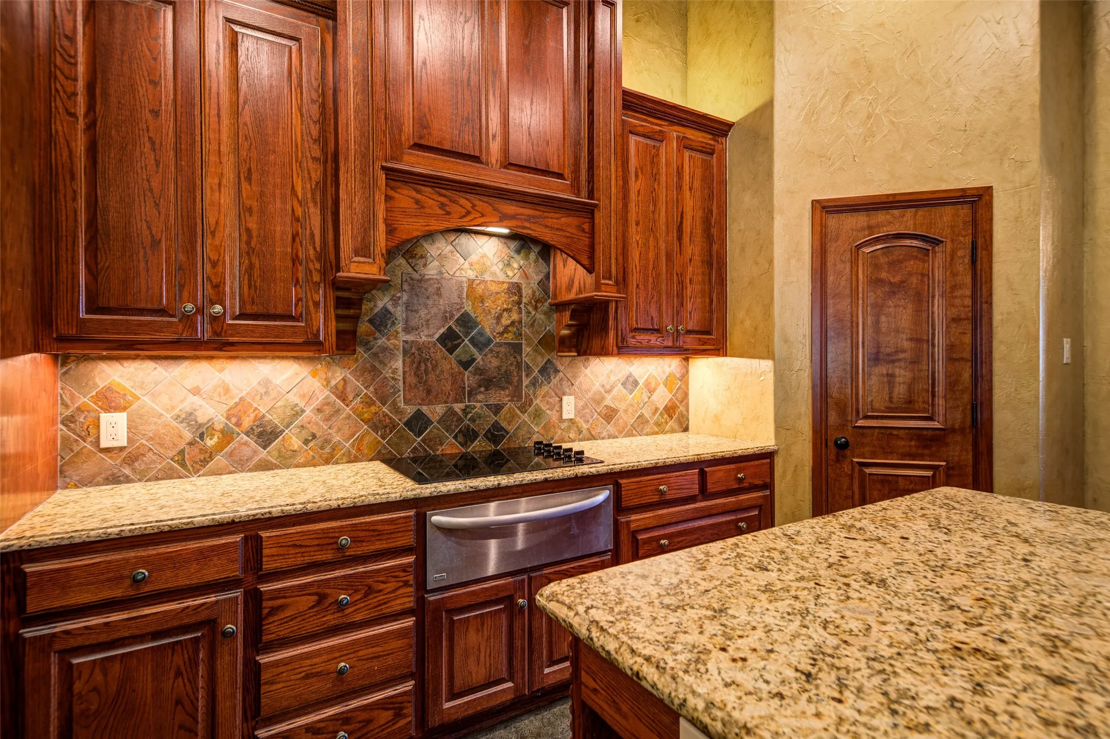 Pantry in kitchen; Expansive kitchen featuring wood cabinetry, stone countertops, and a decorative tile backsplash