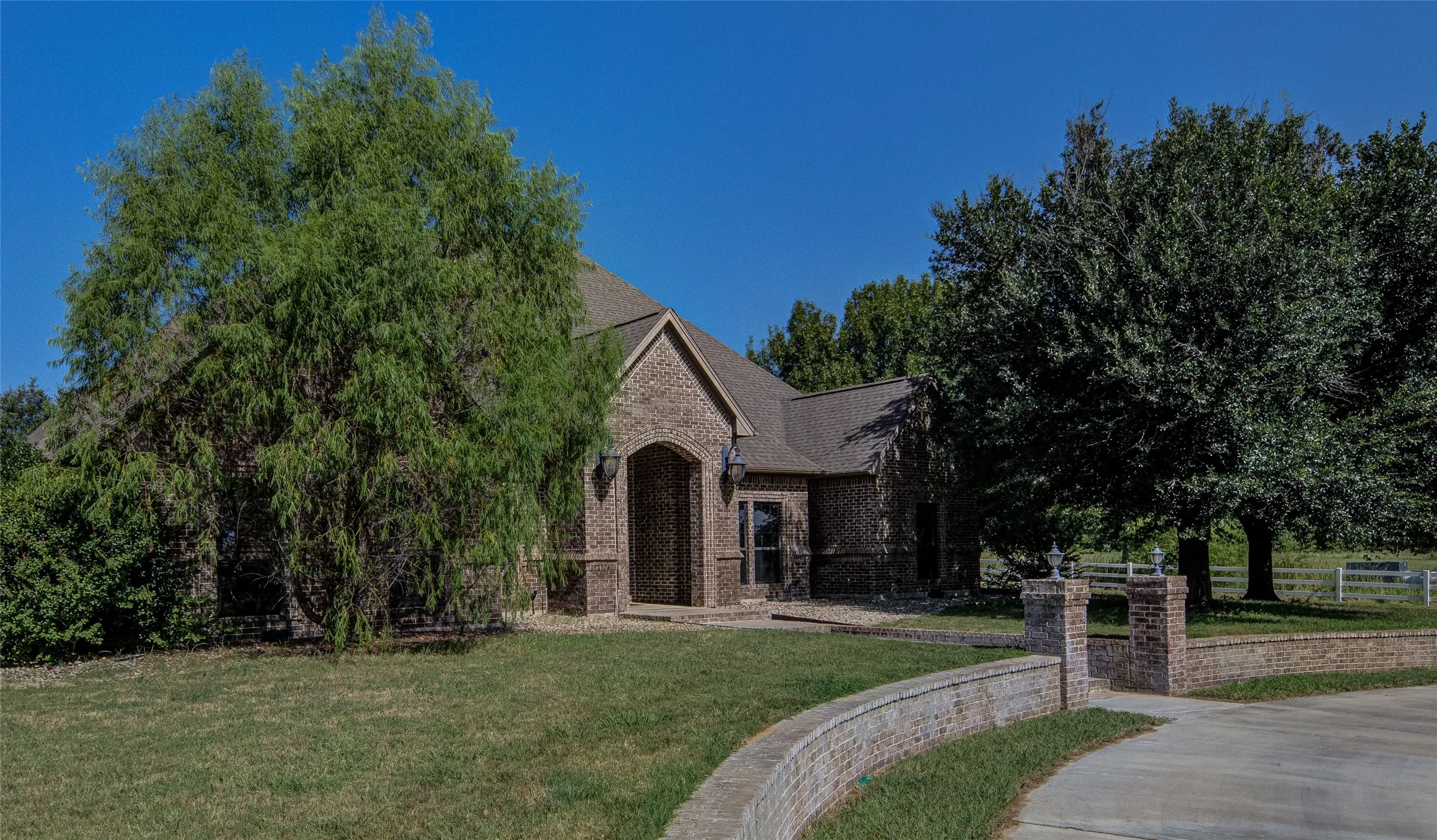Brick exterior featuring an arched entry, a concrete driveway, and a brick retaining wall