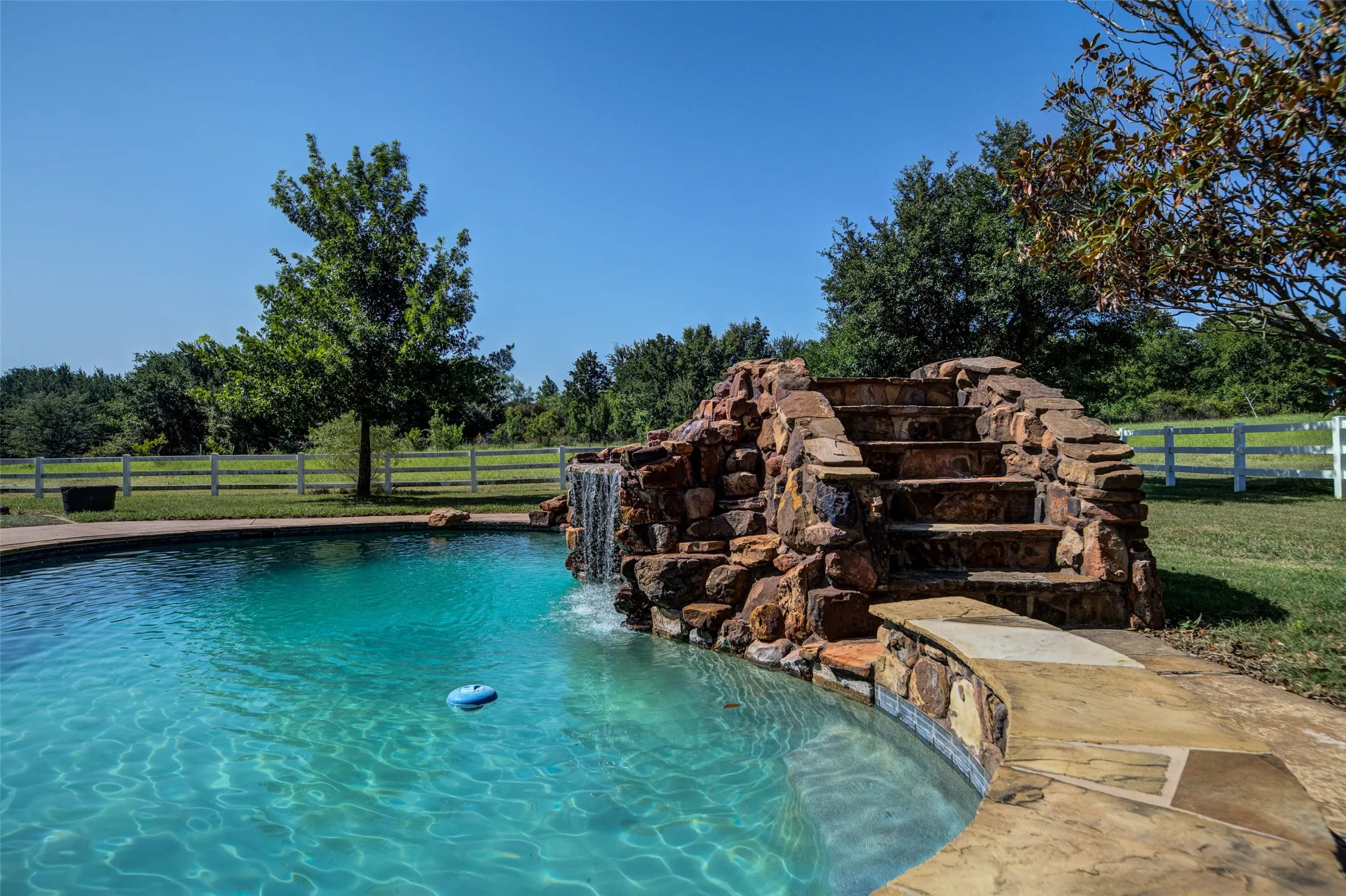 Curved swimming pool featuring a natural rock waterfall and integrated stone steps