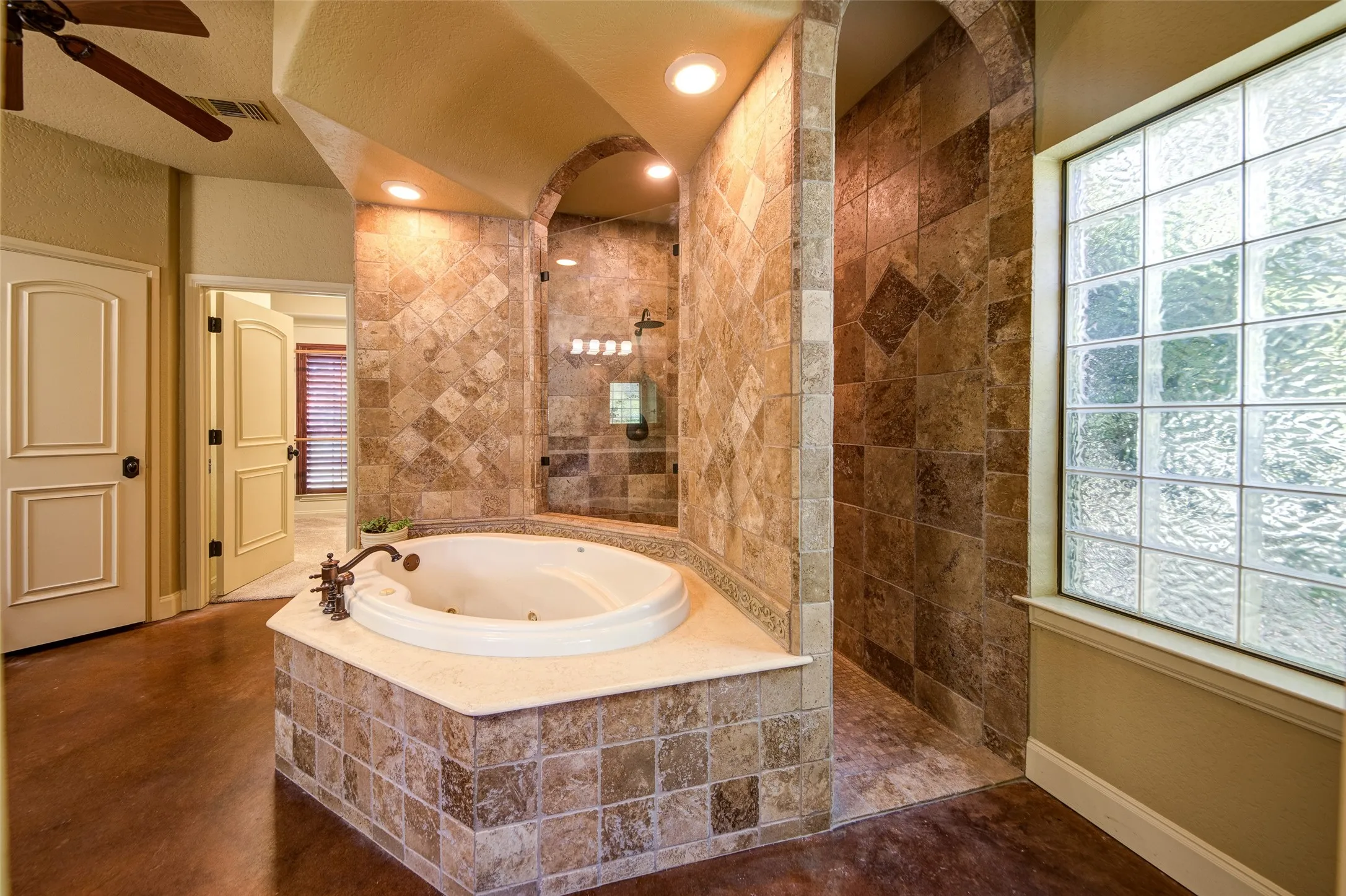 Spa-inspired bathroom featuring a jetted soaking tub with a tiled surround, a glass-enclosed shower with full-height tile, and a large privacy window with glass blocks