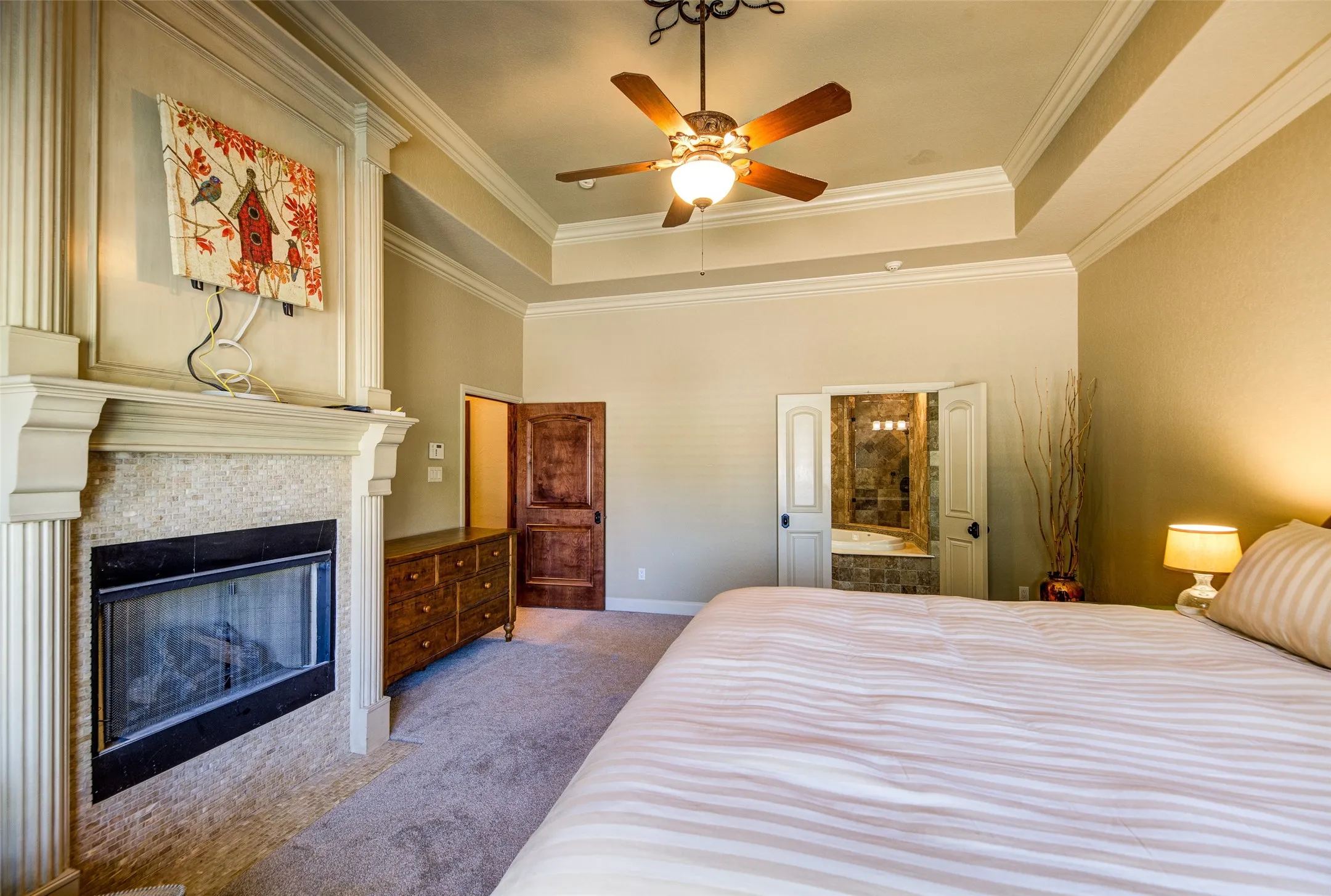 Carpeted room featuring a fireplace with a stone surround, a tray ceiling, and a ceiling fan with integrated lighting