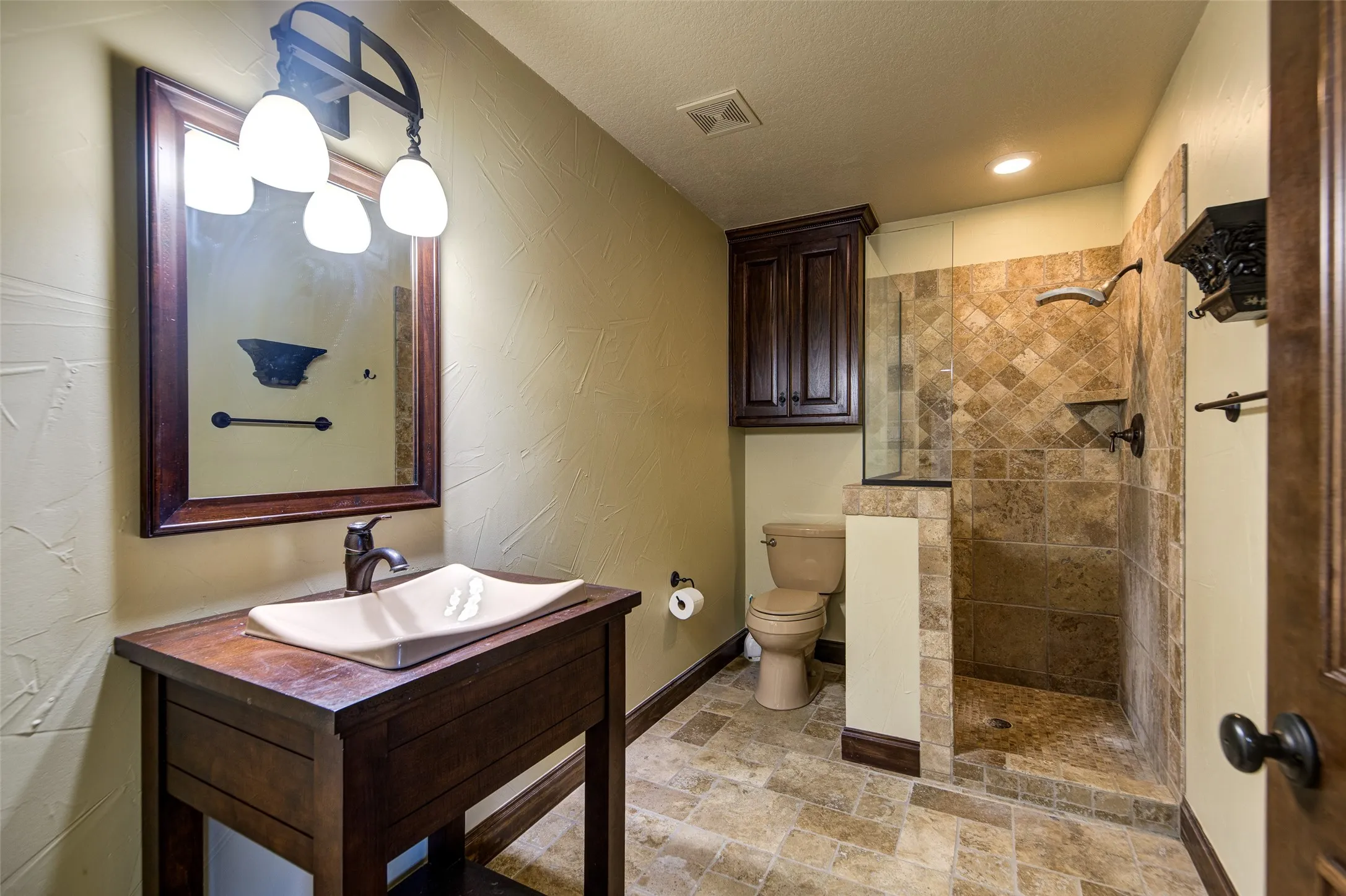 Walk-in shower featuring natural stone tile, glass enclosure, recessed lighting, and integrated shelving