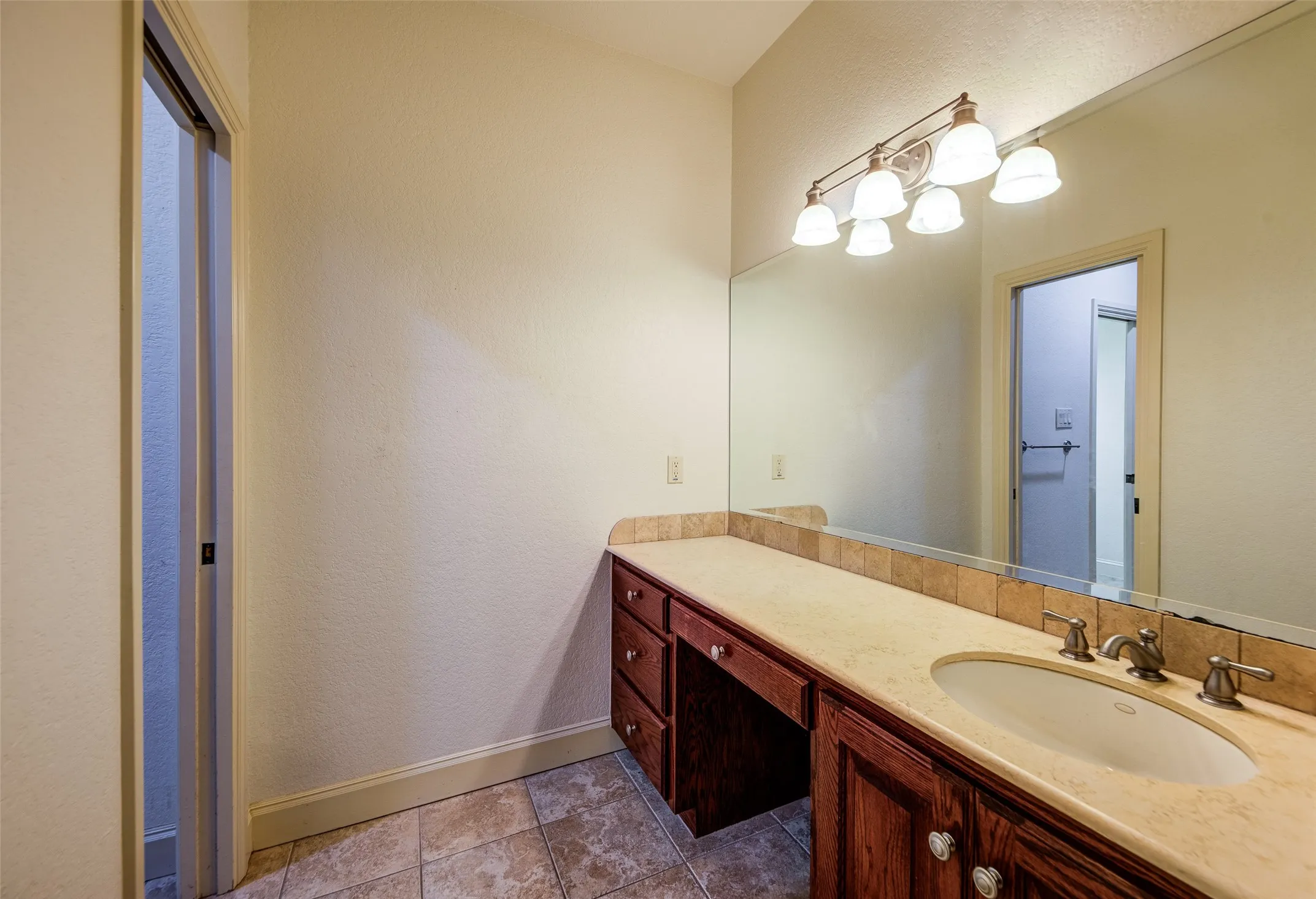 anity area featuring a single basin, ample countertop space, wood-finish cabinetry with decorative hardware, a full-width mirror, and overhead vanity lighting