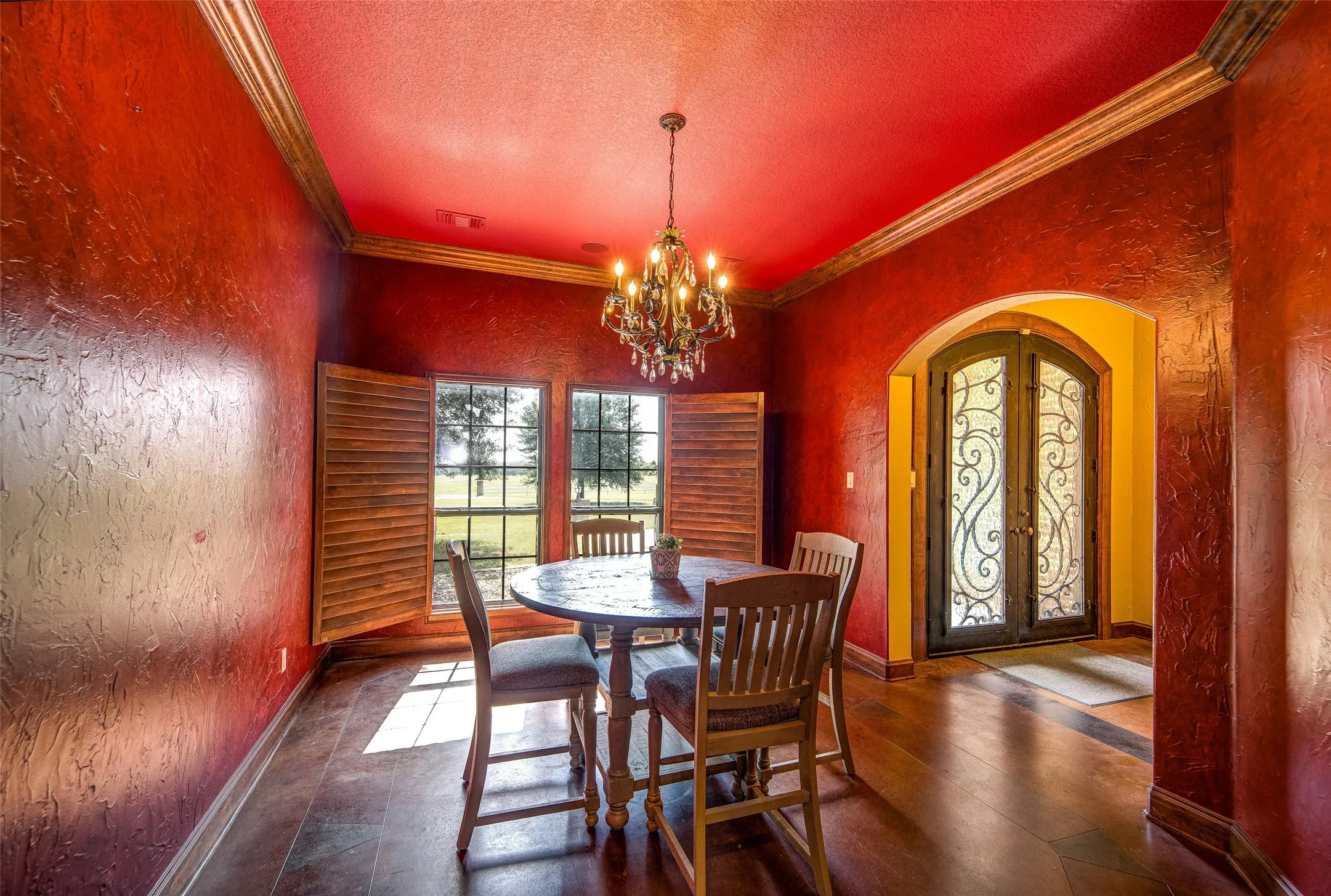 Formal dining space featuring a decorative chandelier, textured red walls with crown molding, and dark wood-finish flooring