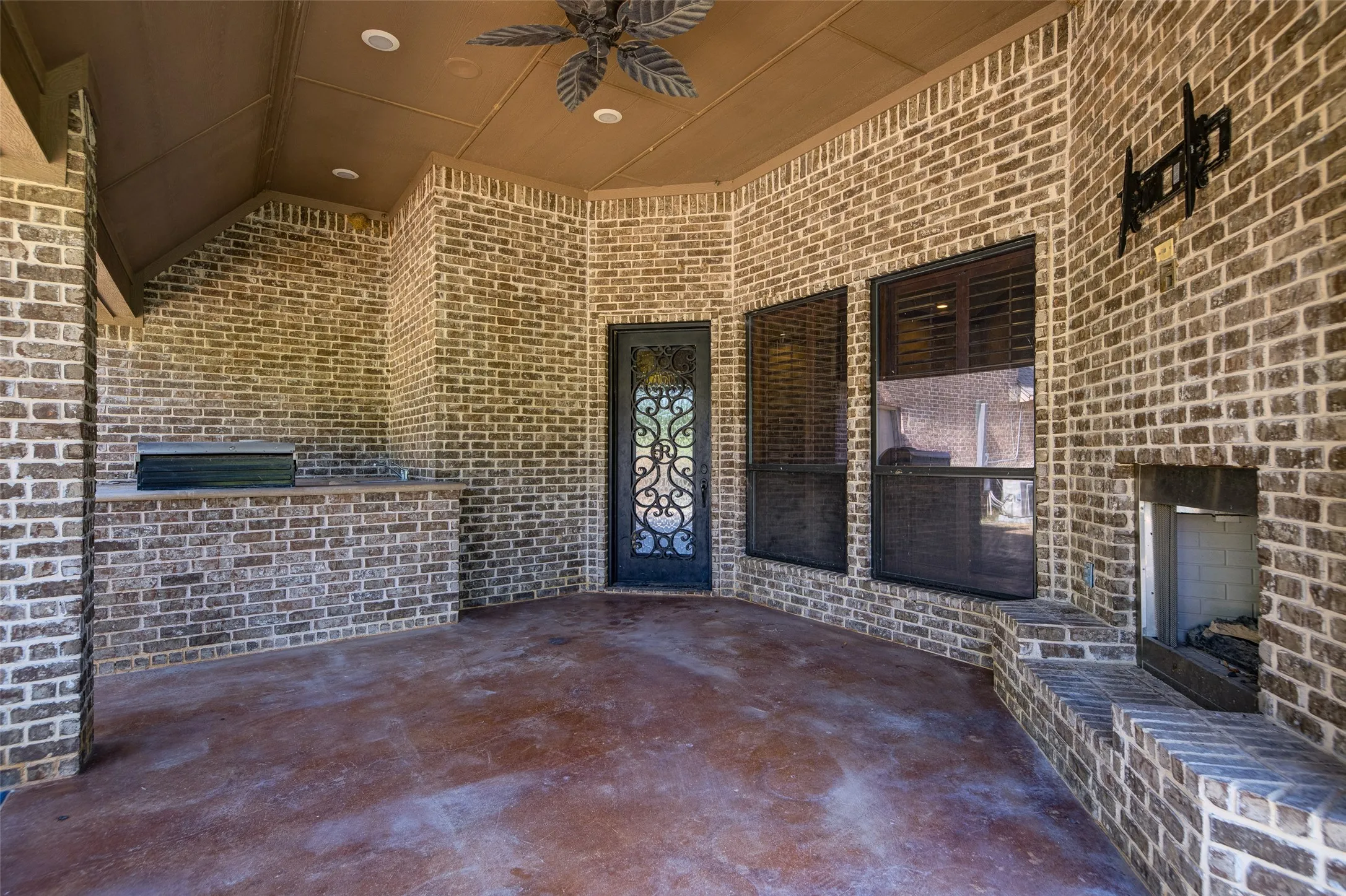 Covered patio featuring extensive brickwork, built-in outdoor kitchen, recessed lighting, ceiling fan, and a fireplace with a stone hearth