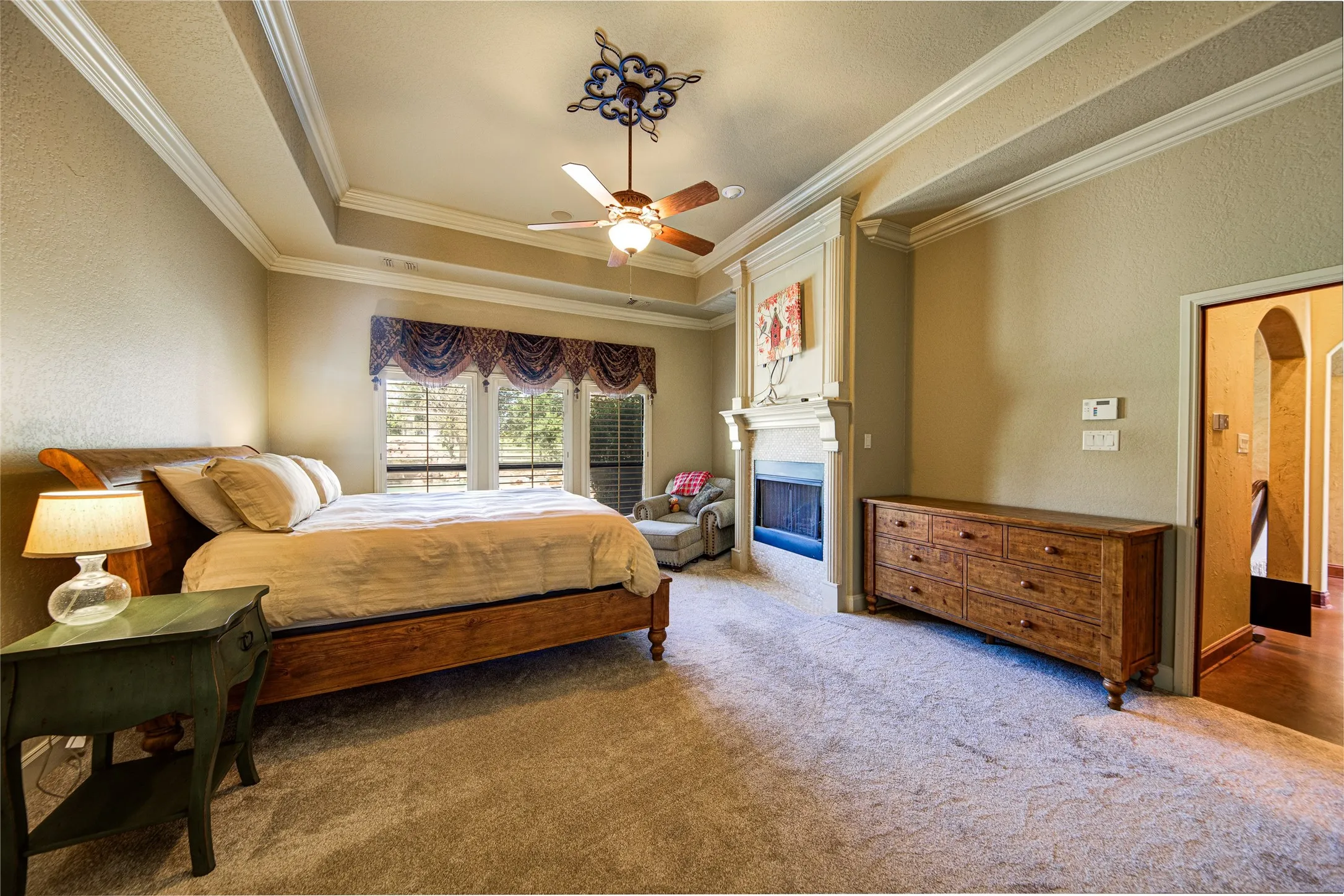 Carpeted room featuring a fireplace with a stone surround, a tray ceiling, and a ceiling fan with integrated lighting