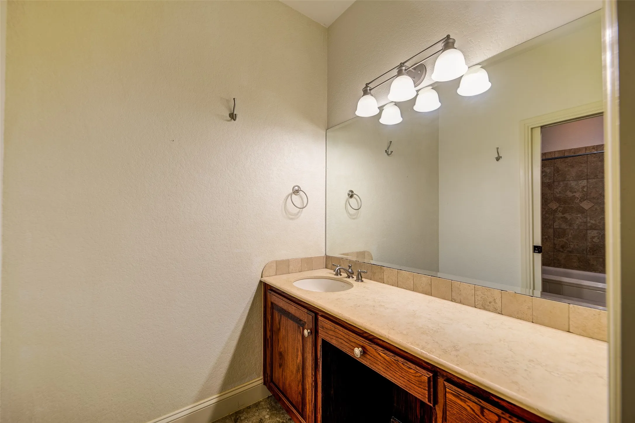Vanity area featuring an integrated sink, polished chrome faucet, wood-finish cabinetry, and a light-toned countertop