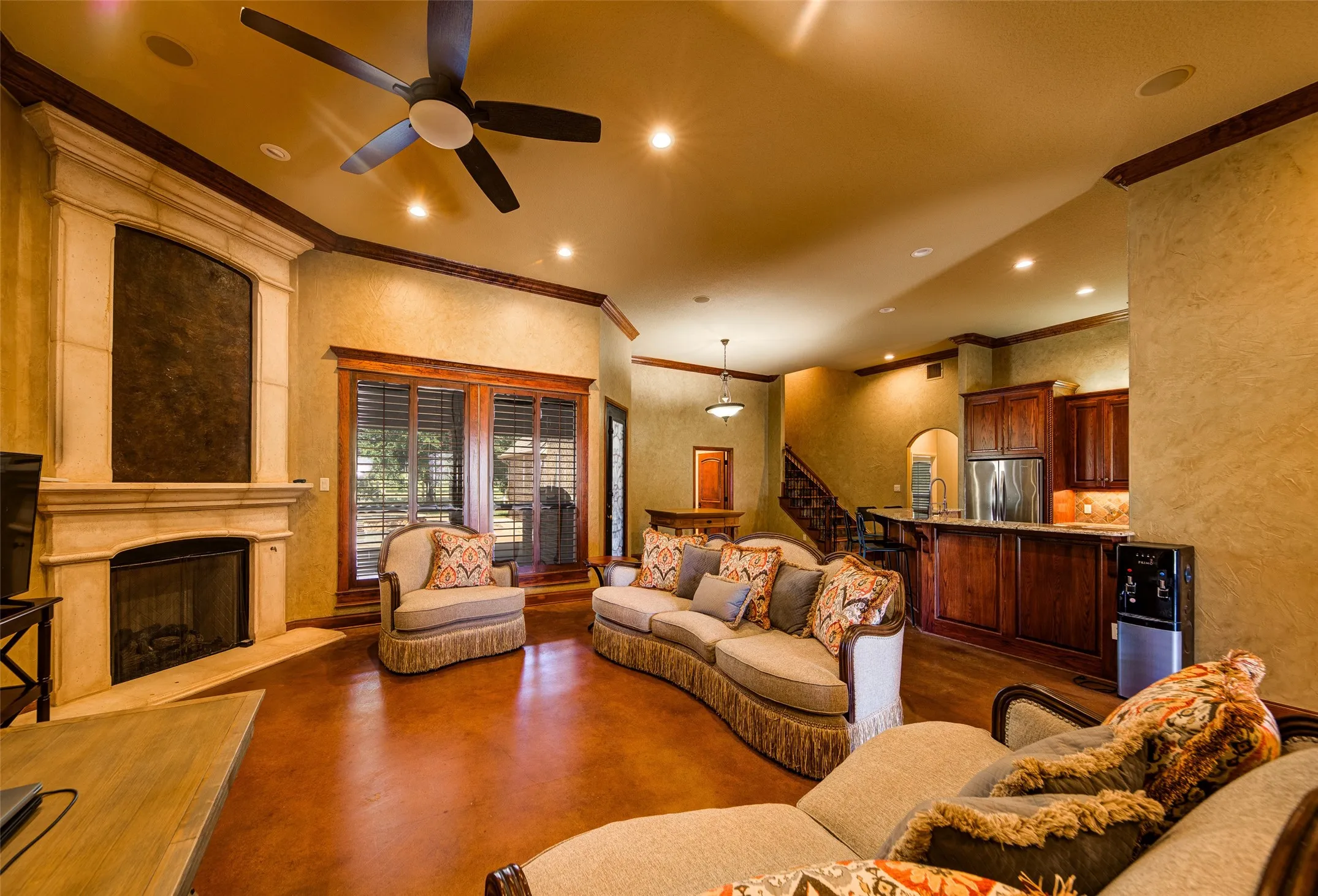 Carpeted room featuring a fireplace with a stone surround, a tray ceiling, and a ceiling fan with integrated lighting