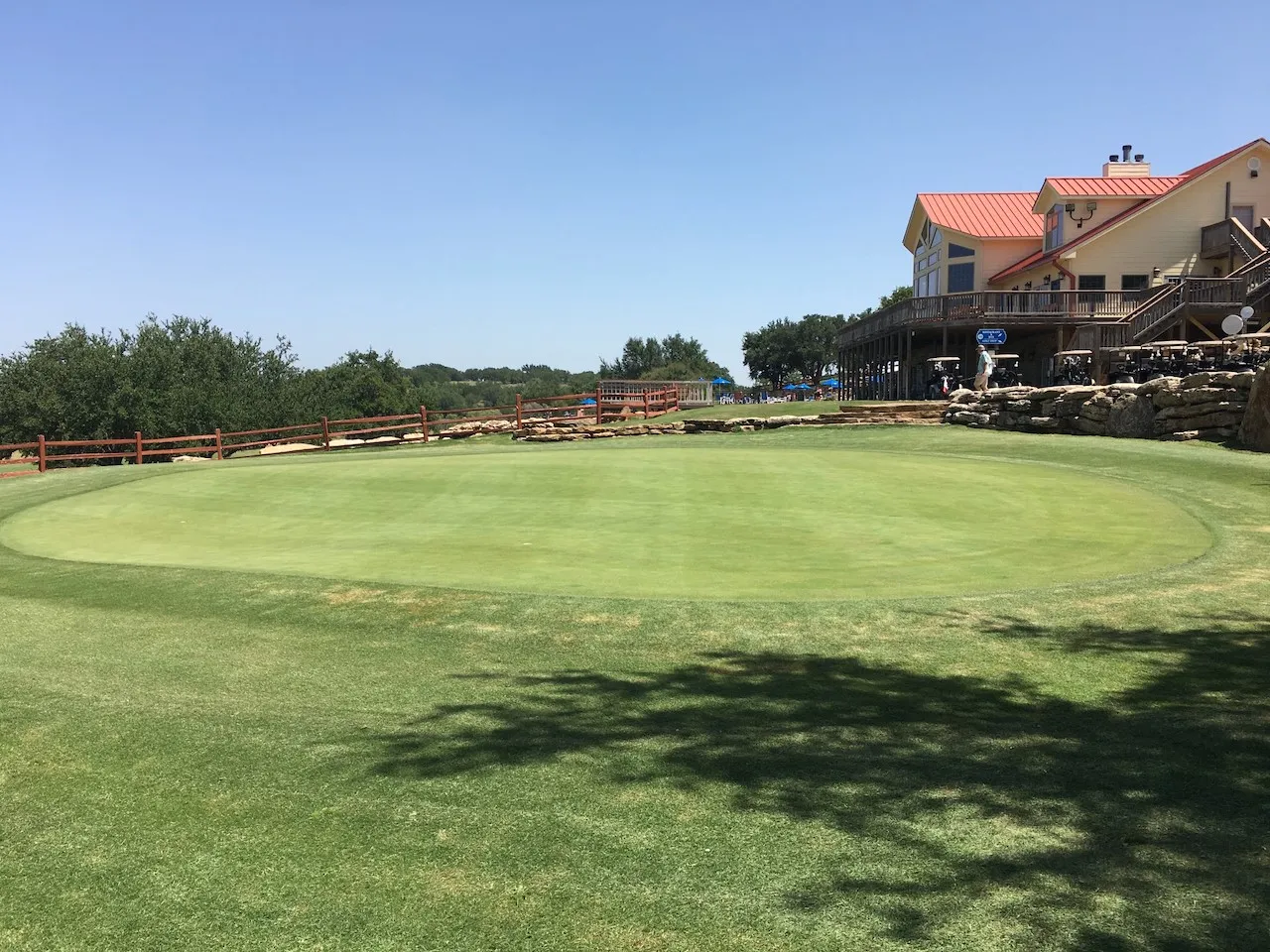 Manicured putting green with a distant multi-level building featuring a red roof and expansive wooden deck