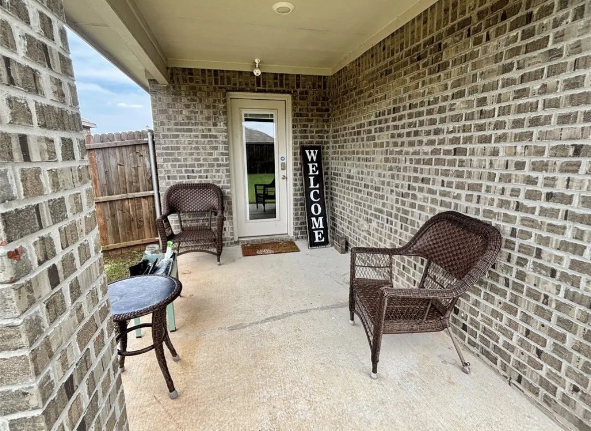 Covered patio featuring brick exterior, concrete flooring, exterior lighting, and a full-light rear entry door