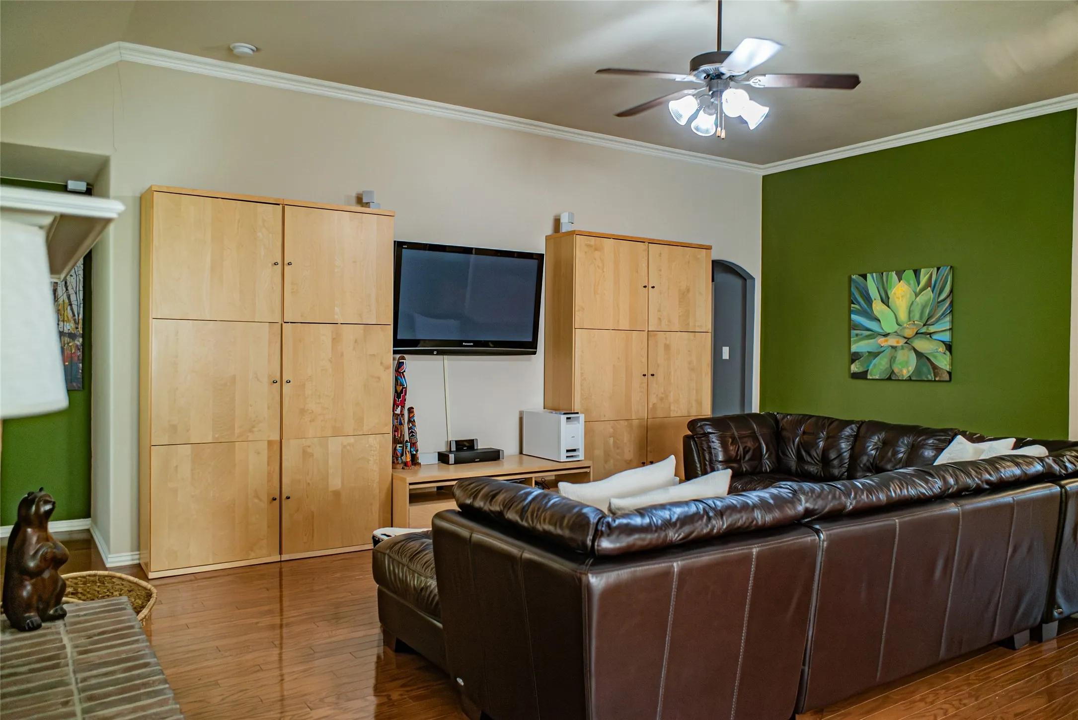 Living area featuring wood-finish flooring, crown molding, a ceiling fan with integrated lighting, and a prominent accent wall