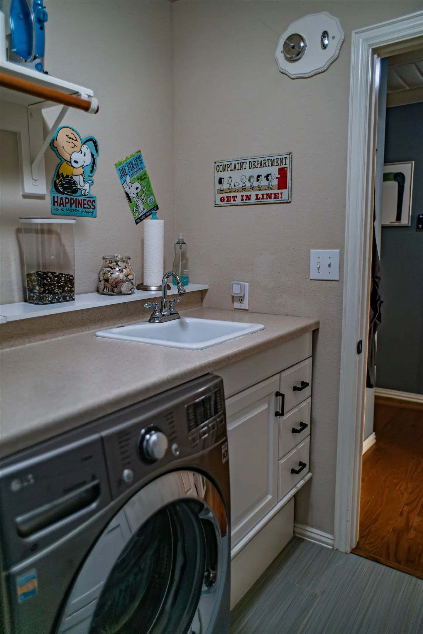 Utility room featuring a built-in sink with chrome faucet, light-toned countertop, white cabinetry with dark hardware, and light gray wood-finish flooring
