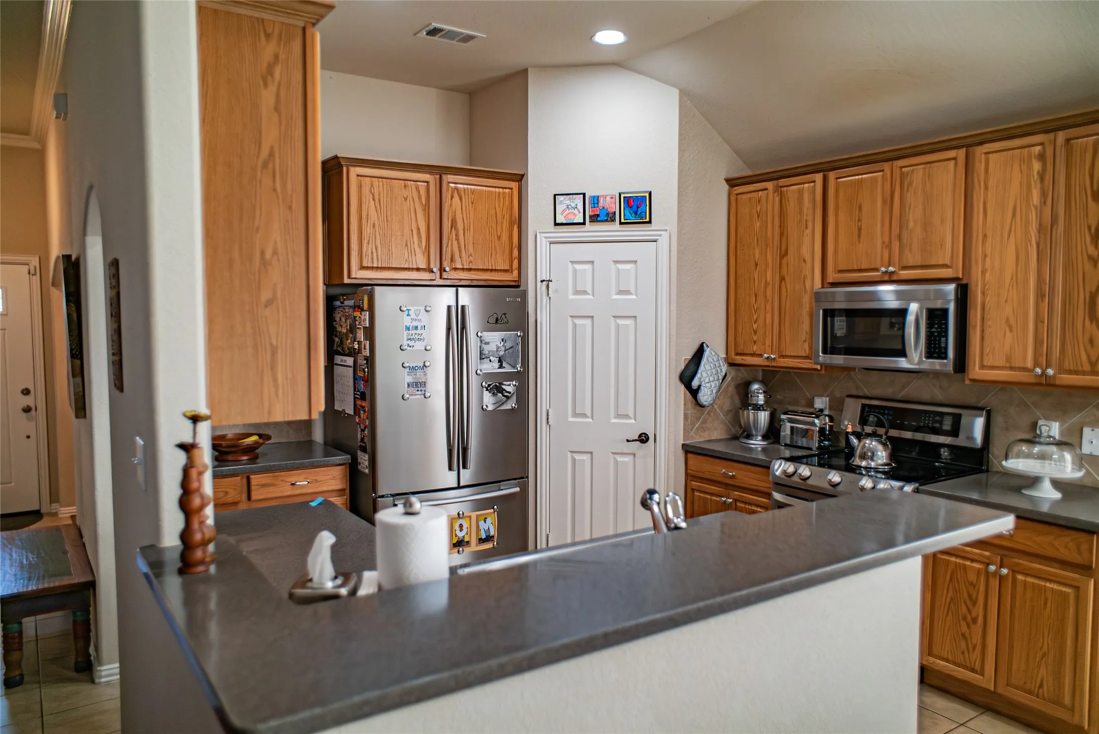 Open-concept kitchen featuring wood cabinetry, stainless steel appliances, dark countertops, and a tiled backsplash